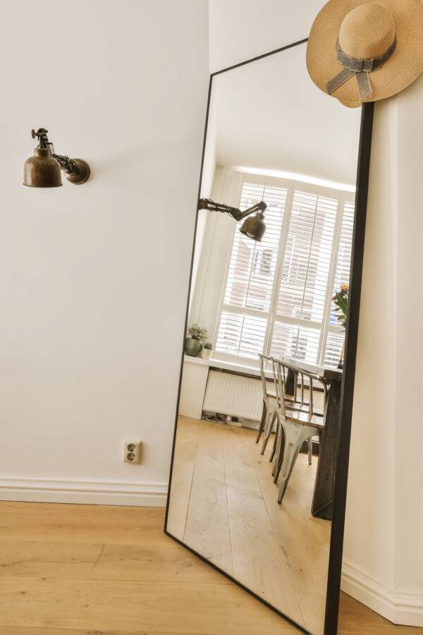 A mirror leaning against a wall, a table and chairs visible in its reflection.