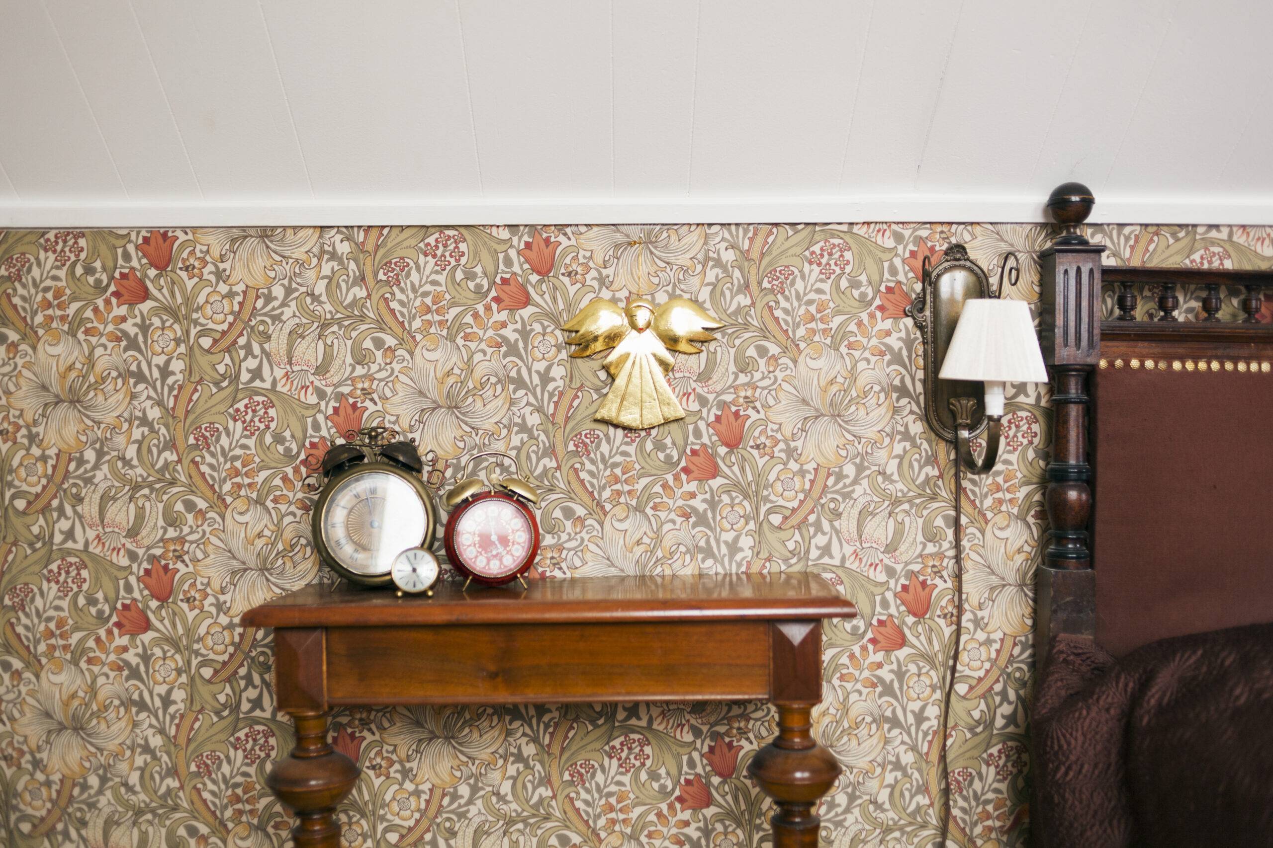 A bedroom wall with detailed floral wallpaper, a side table and bed also visible.