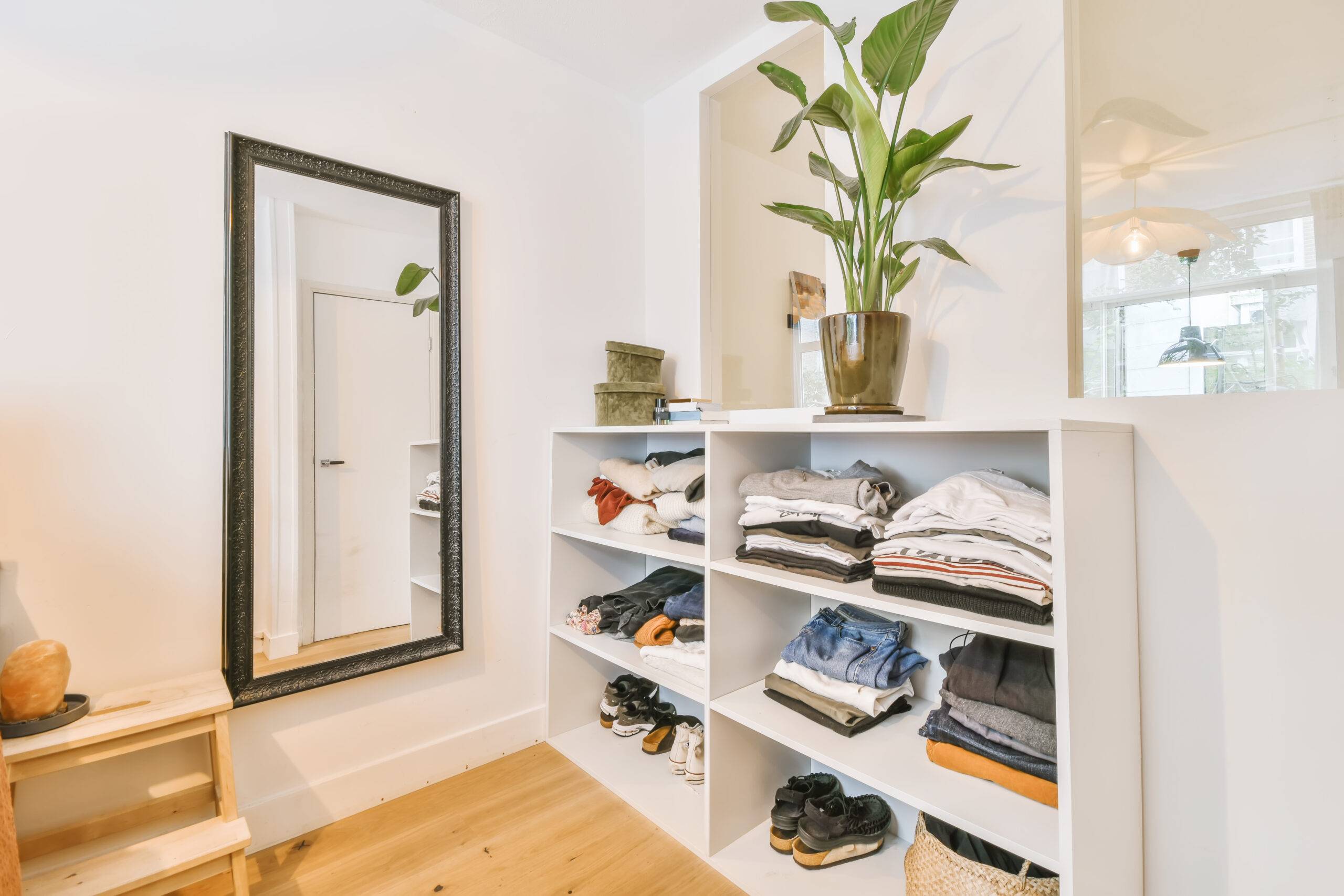 Bookshelves with folded clothes in it, a mirror on the wall.