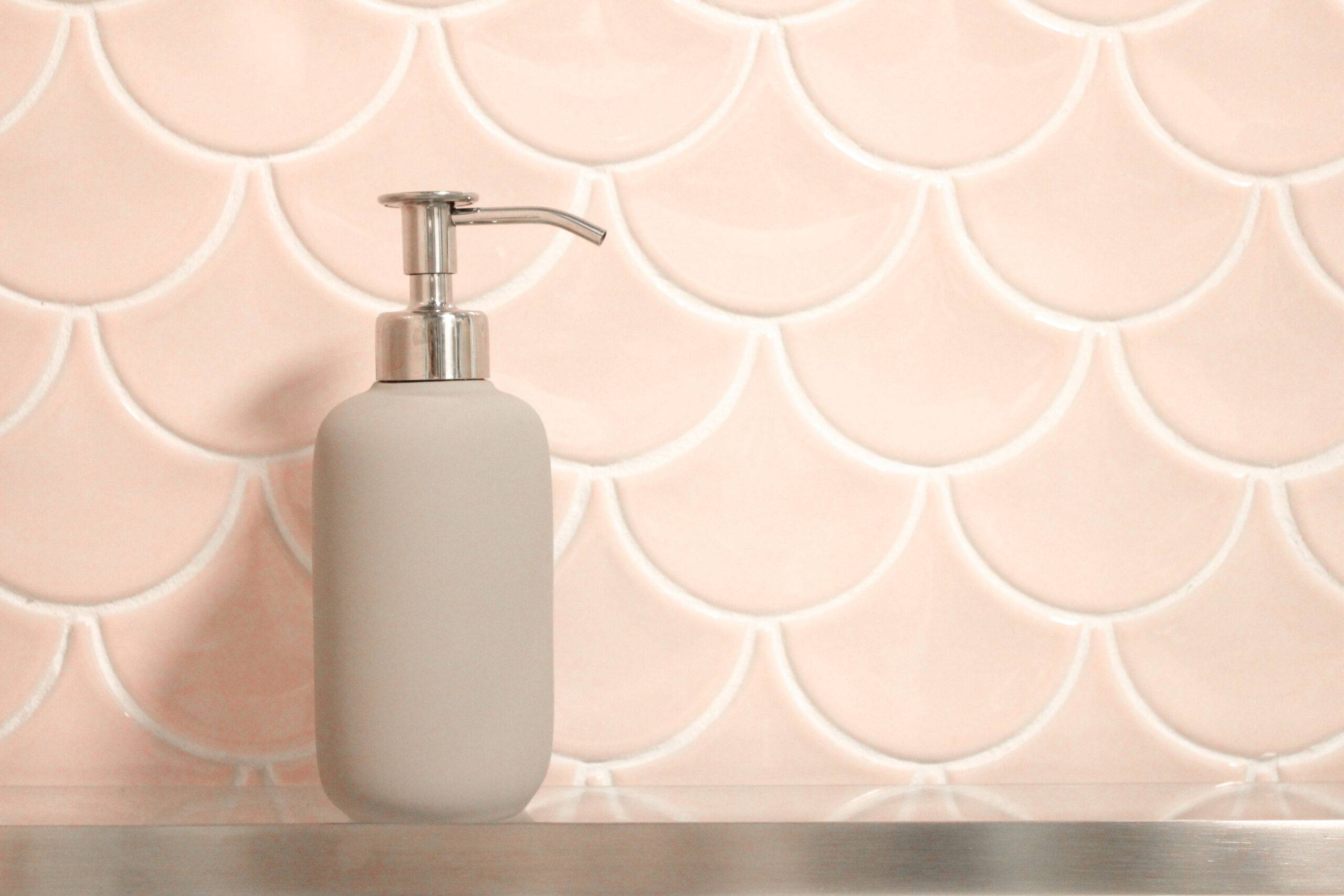 Scalloped tiles with a soap dispenser in front.