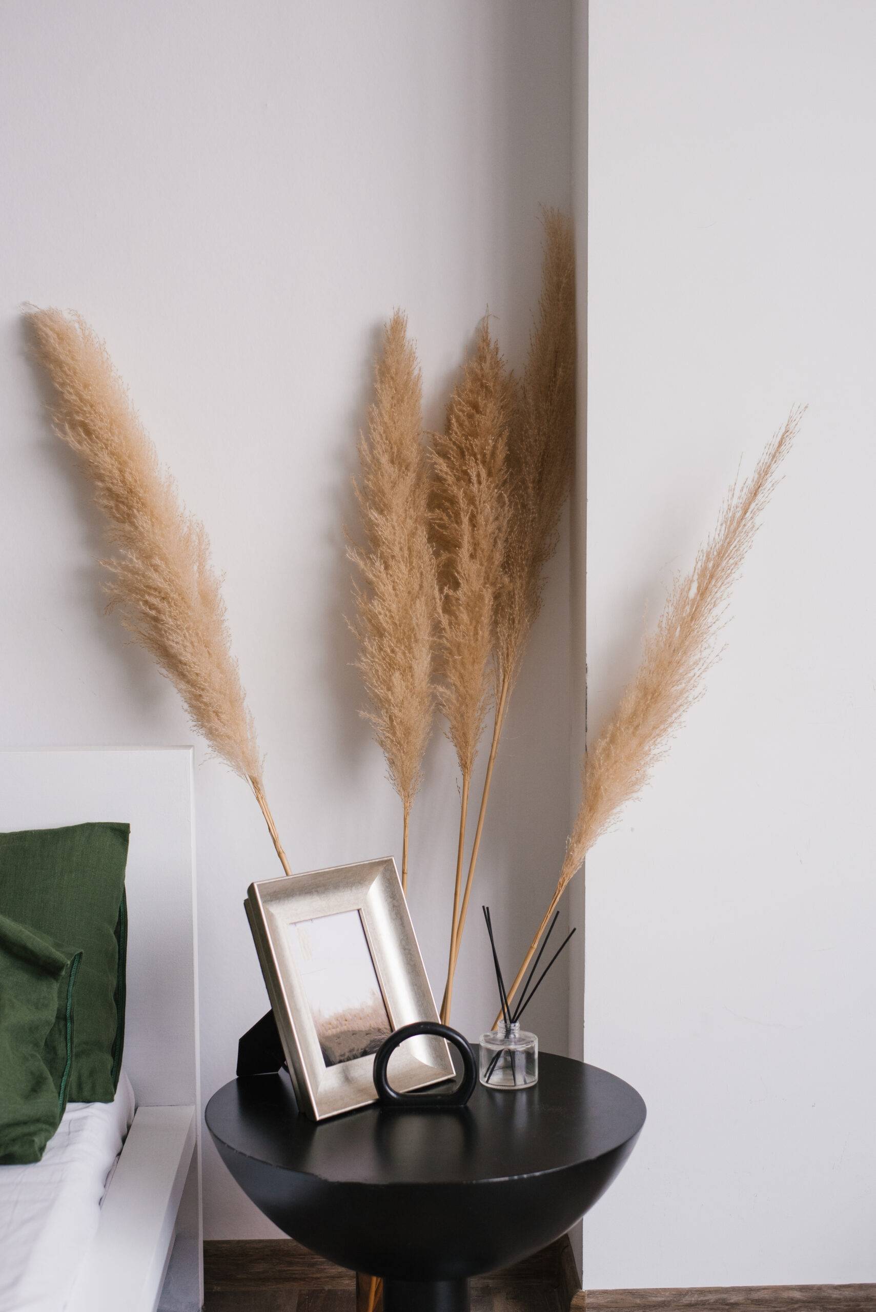 Tall pampas grass stalks behind a night table, a bed beside it.