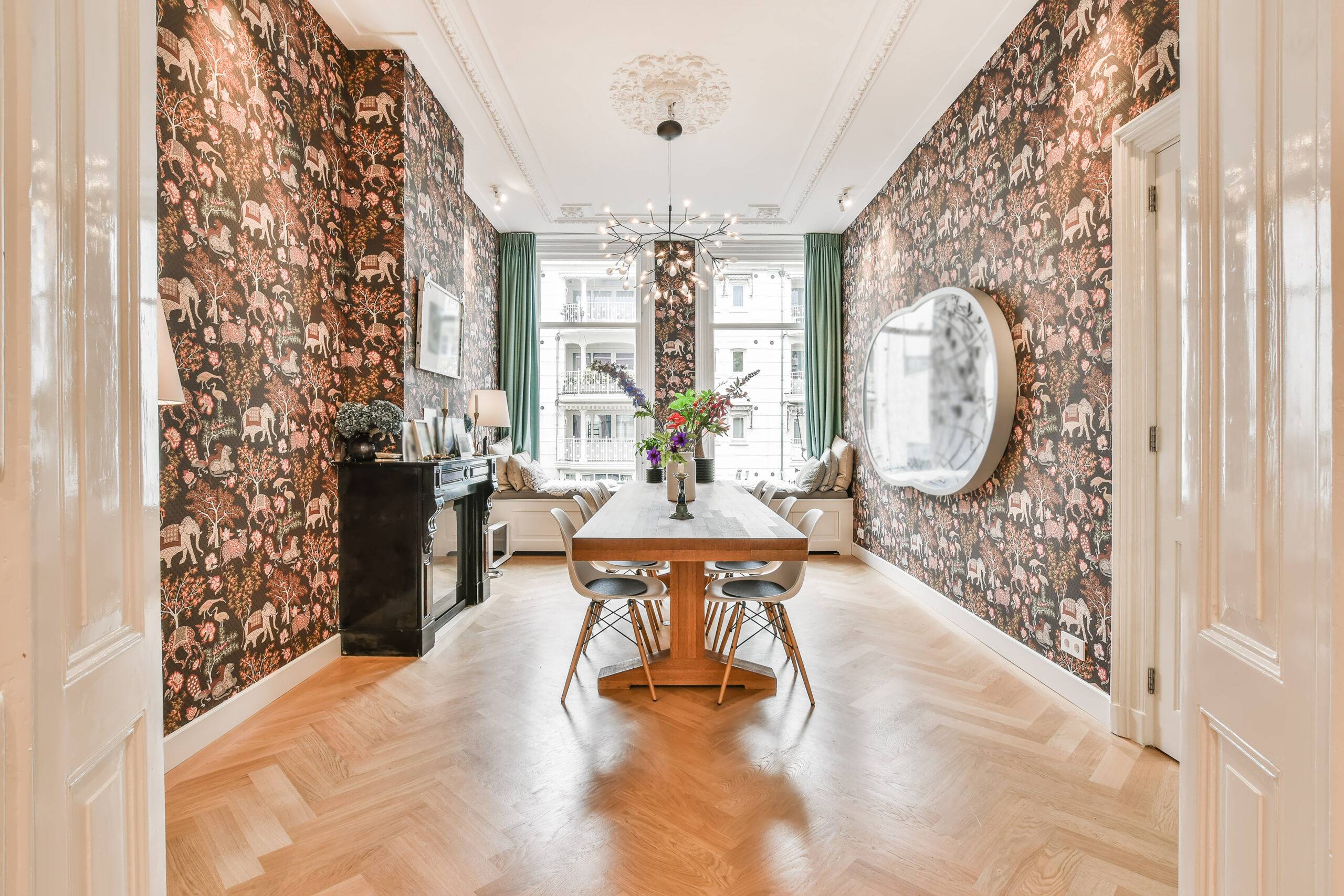 A dining room with ornate wallpaper and bright windows at the end.