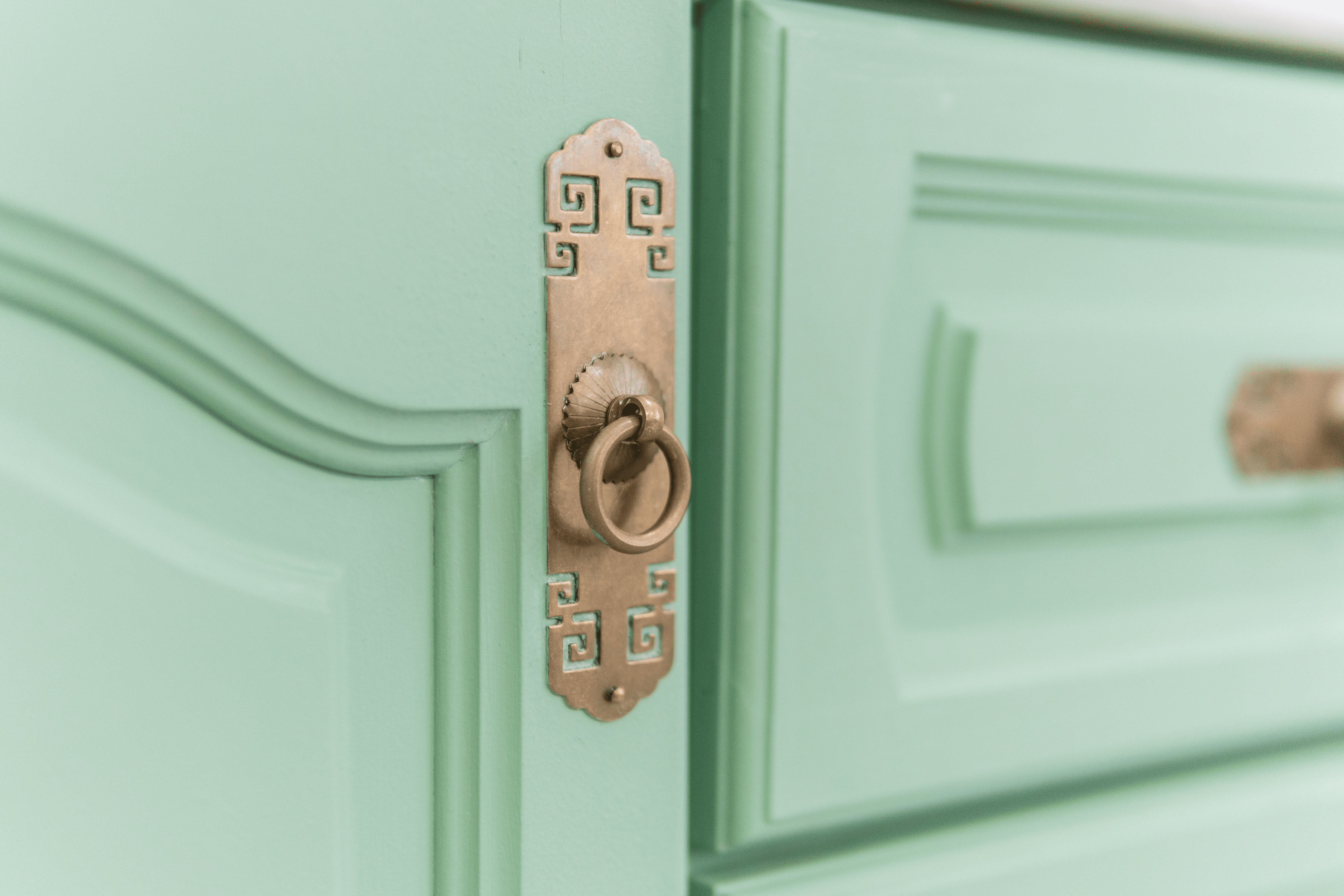 A closeup of a fancy gold drawer pull on a mint green cabinet door.