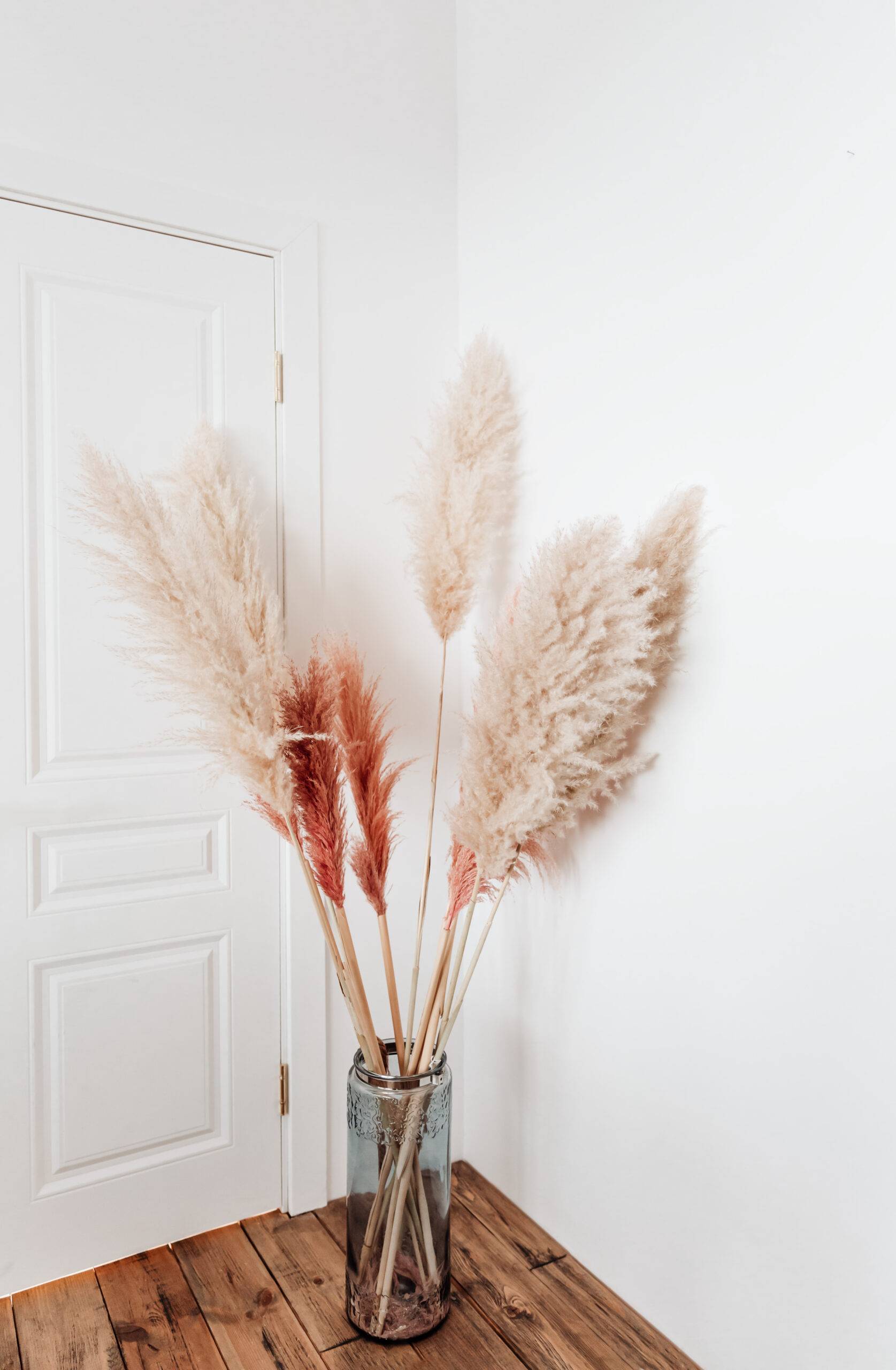 Tall stalks of pampas grass in a vase on the ground beside a door.