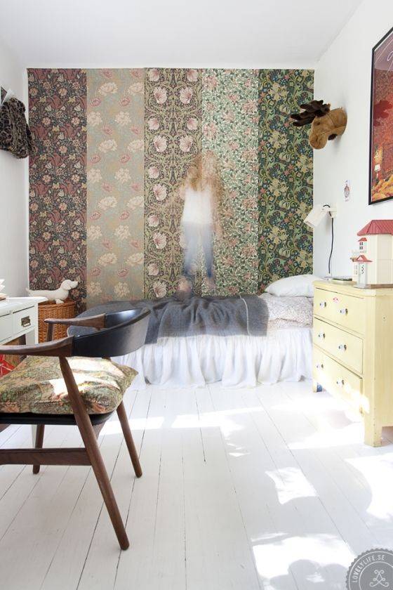 A bedroom with a feature wall of multiple wallpapers, a blurred little girl jumping on the bed.