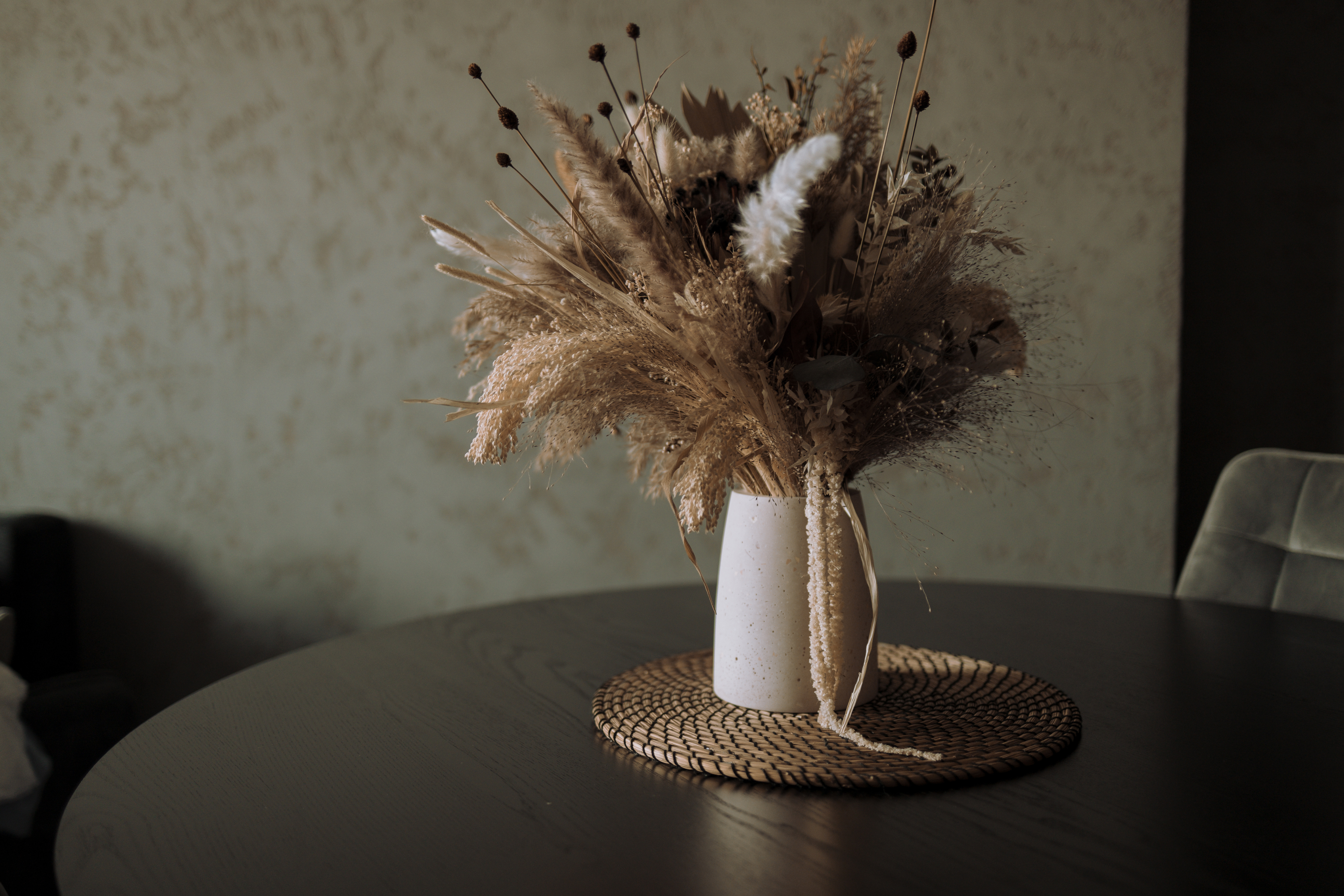 A vase on a table filled with pampas grass and other dried plants.