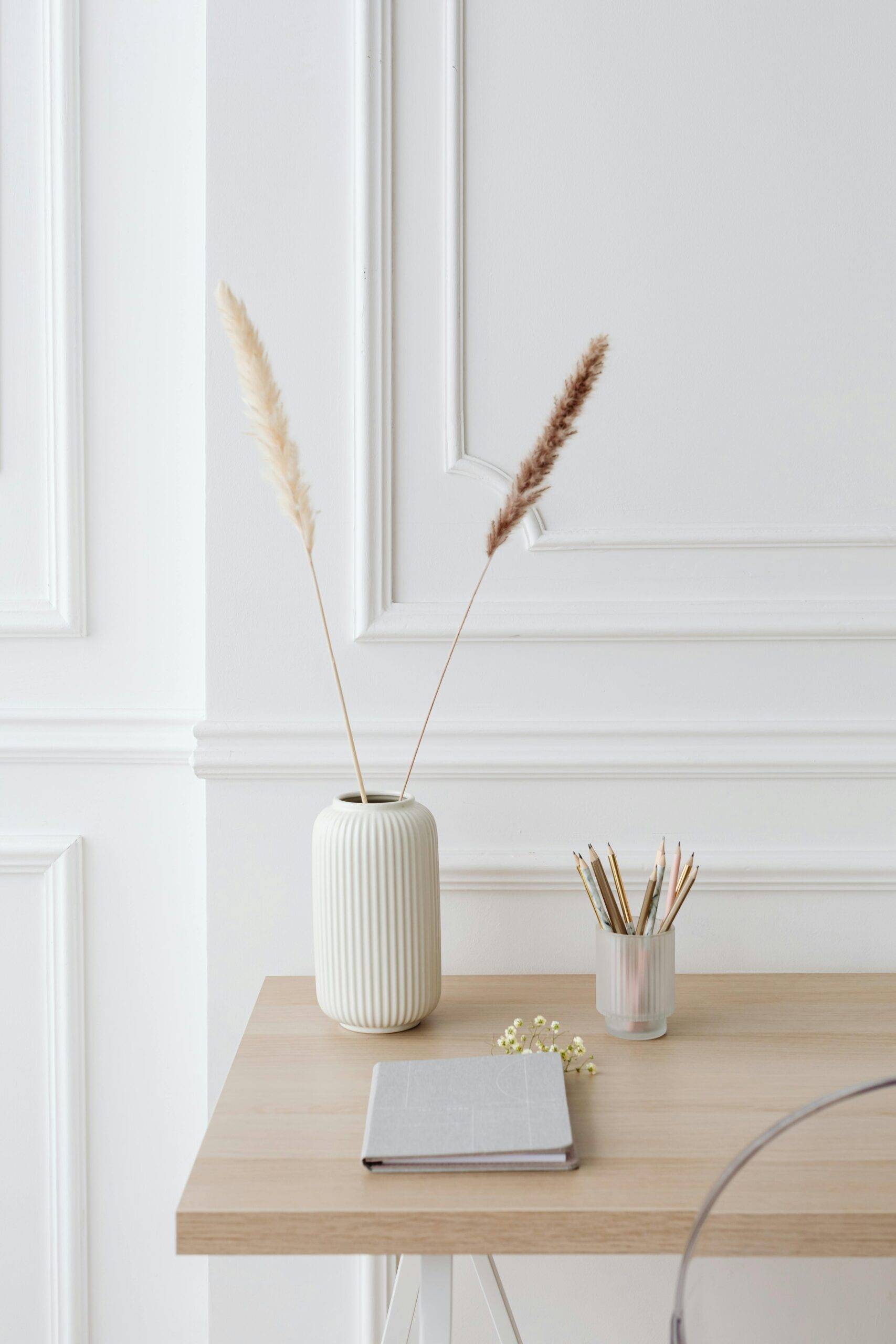 Two single stocks of pampas grass in a vase on a desk.