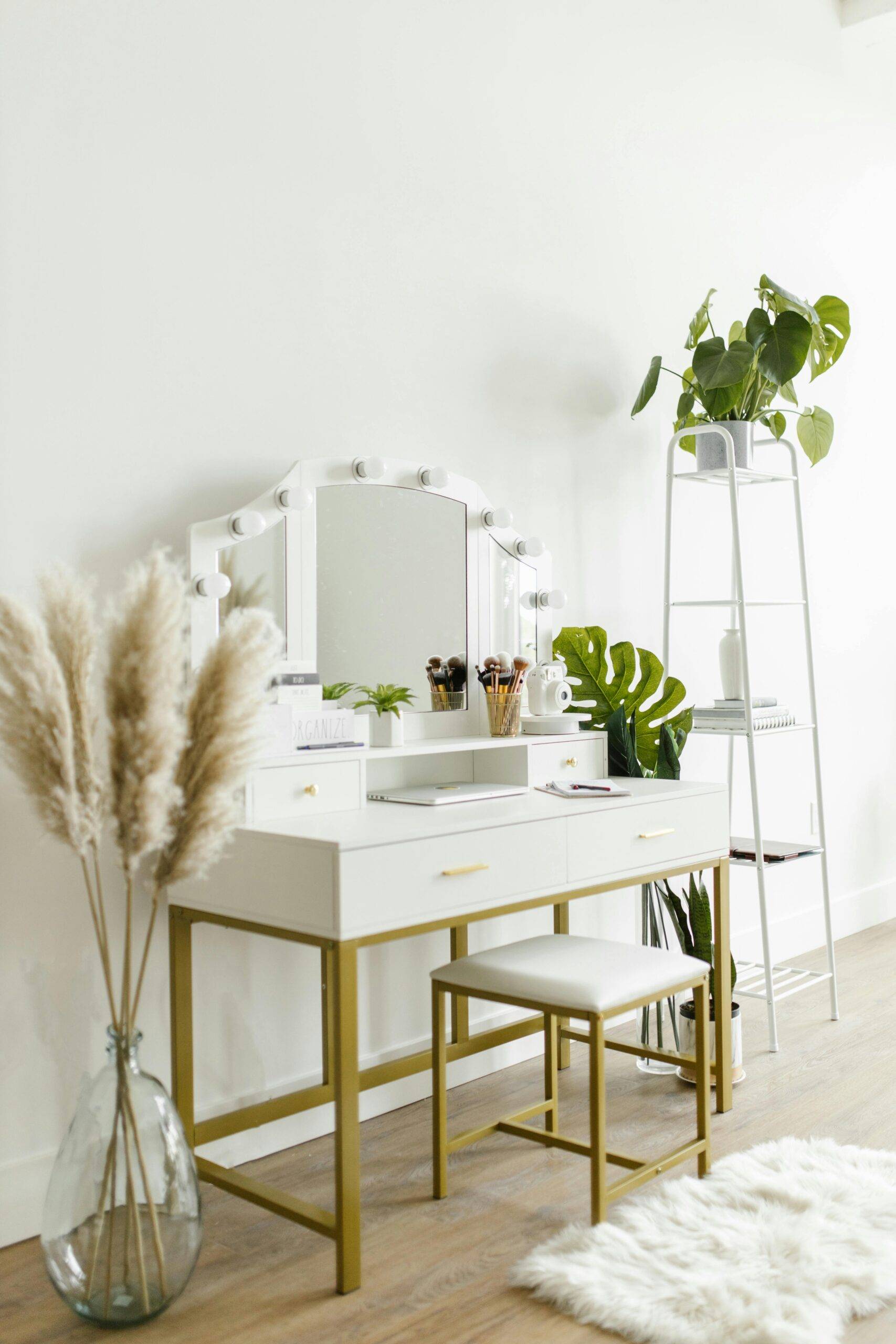 Pampas grass in a vase on the ground beside a vanity table.