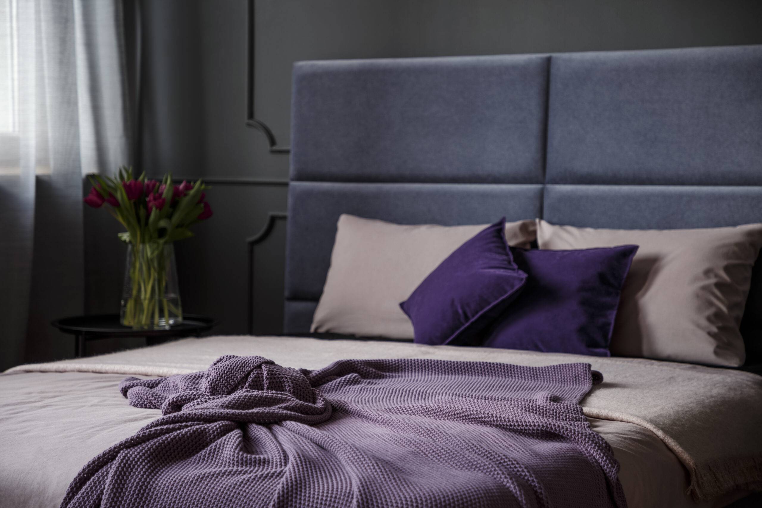 Close-up of violet blanket on bed in feminine bedroom interior with flowers