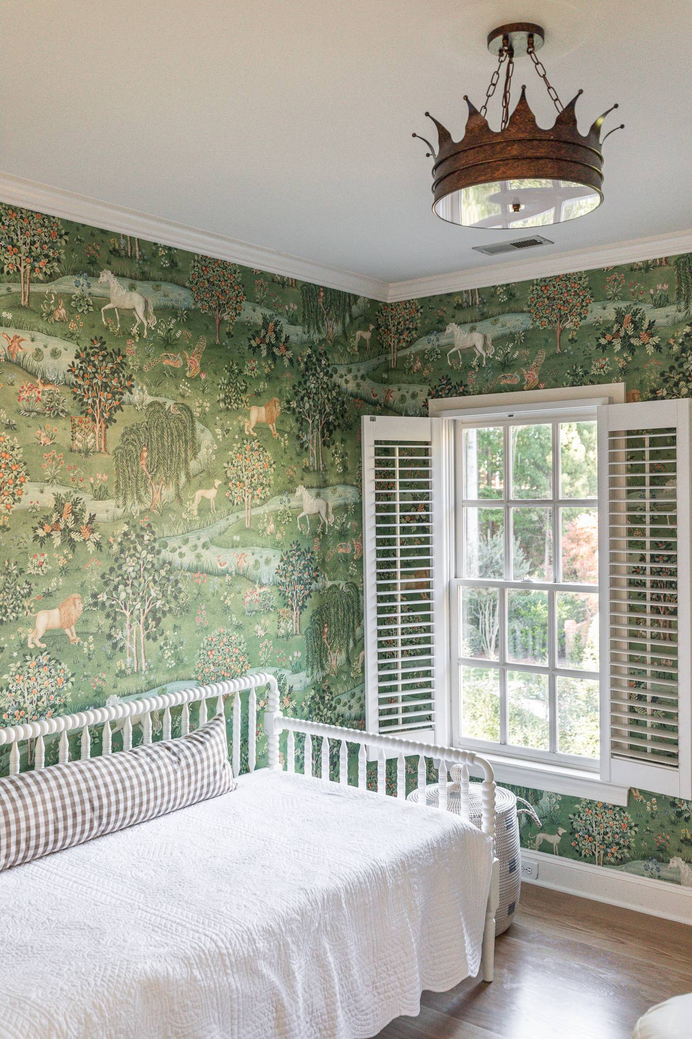 A bedroom with whimsical wallpaper, a bright window, bed, and statement lighting.