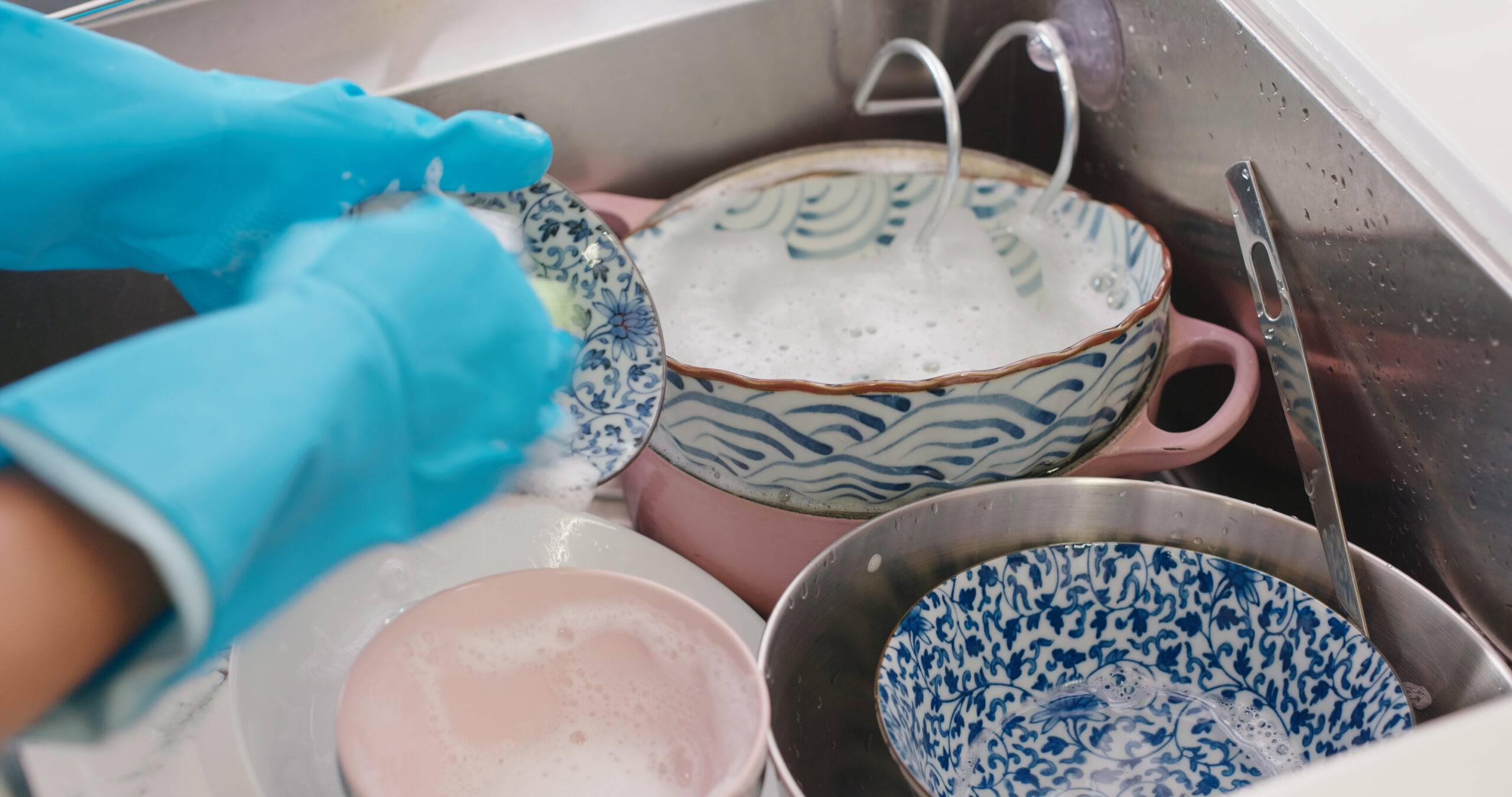 Gloved hands washing dishes, more dishes in the sink.