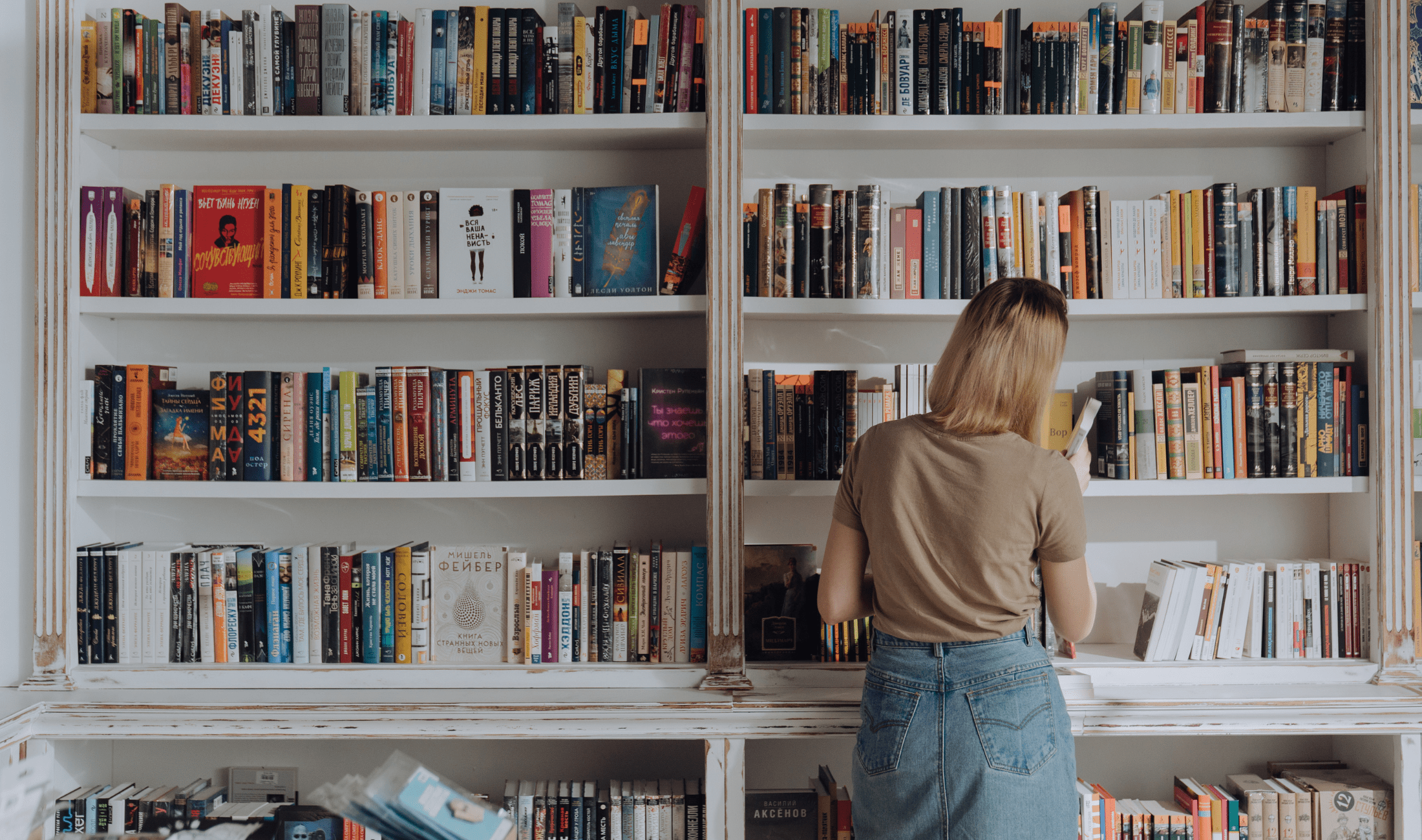 A woman standing in front of a full wall-sized white bookshelf unit.