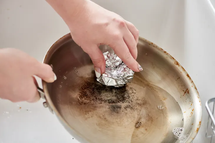 Someone using a balled up piece of tin foil to scrub at a pan.