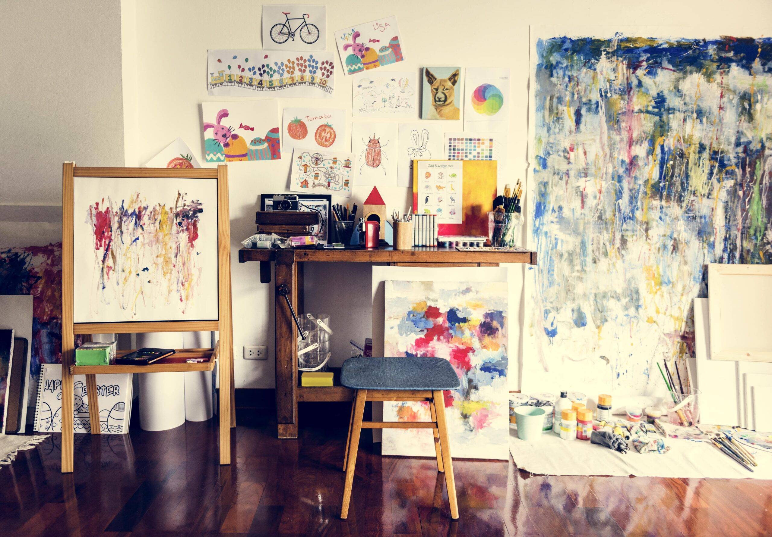 A painter's studio corner, a work desk, easel, stool, and other previous artworks scattered about.