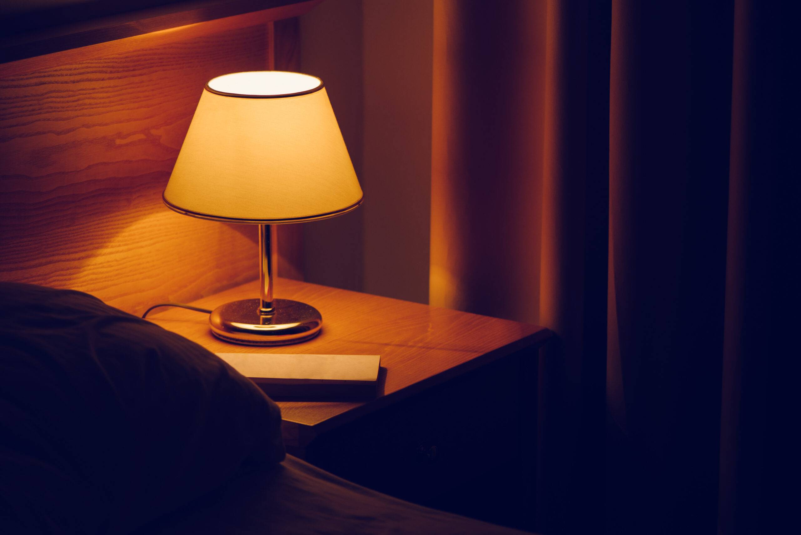 Light bulb and book on bedside table in bedroom, selective focus