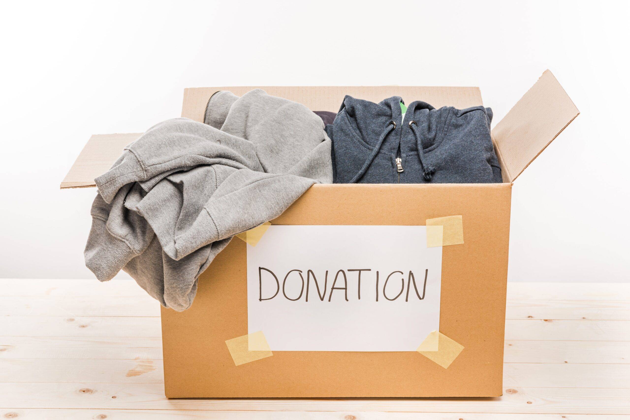 A cardboard box with a label that reads, "Donation" on it, the box full of clothes.