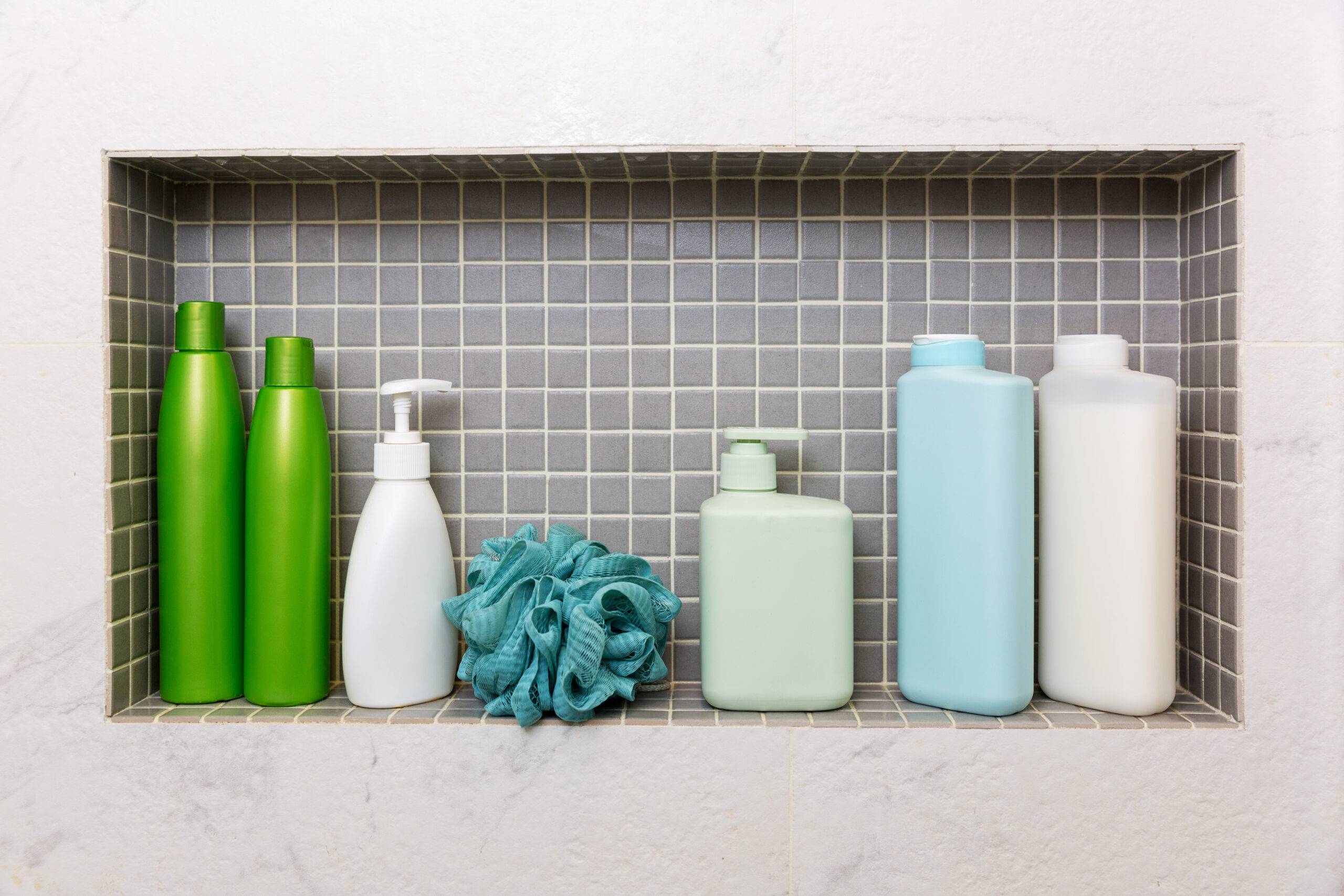 A recessed shower shelf with gray tile and various shampoo bottles.