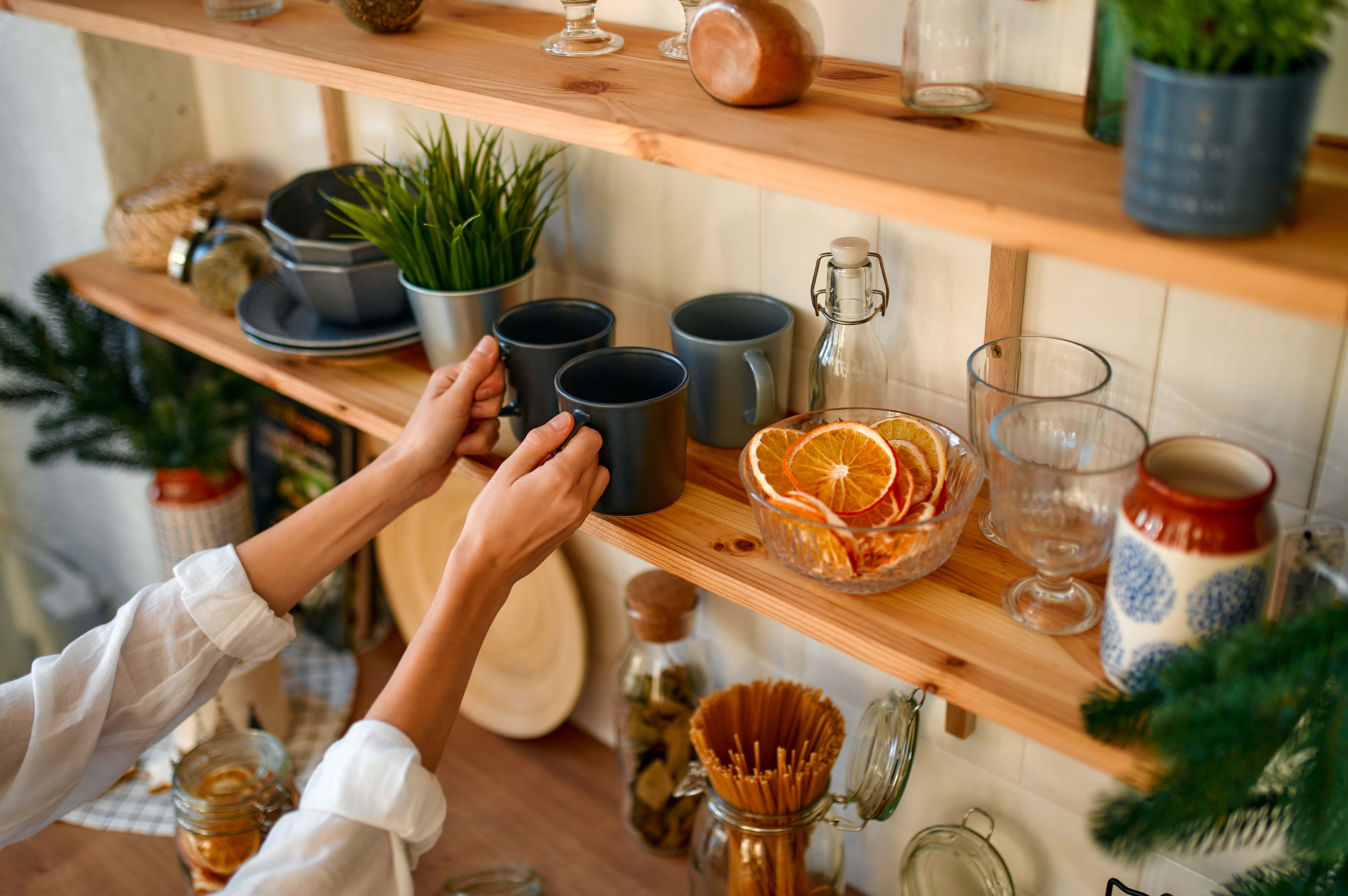 Une série de longues unités d'étagères murales remplies de tasses, de verres et d'autres articles de décoration, un poil de mains tendant la main pour saisir deux tasses.