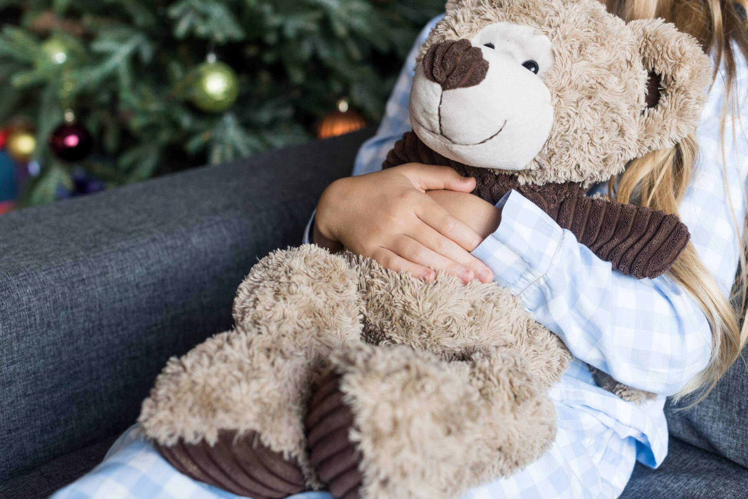 cropped shot of child hugging teddy bear and sitting on couch at christmas time