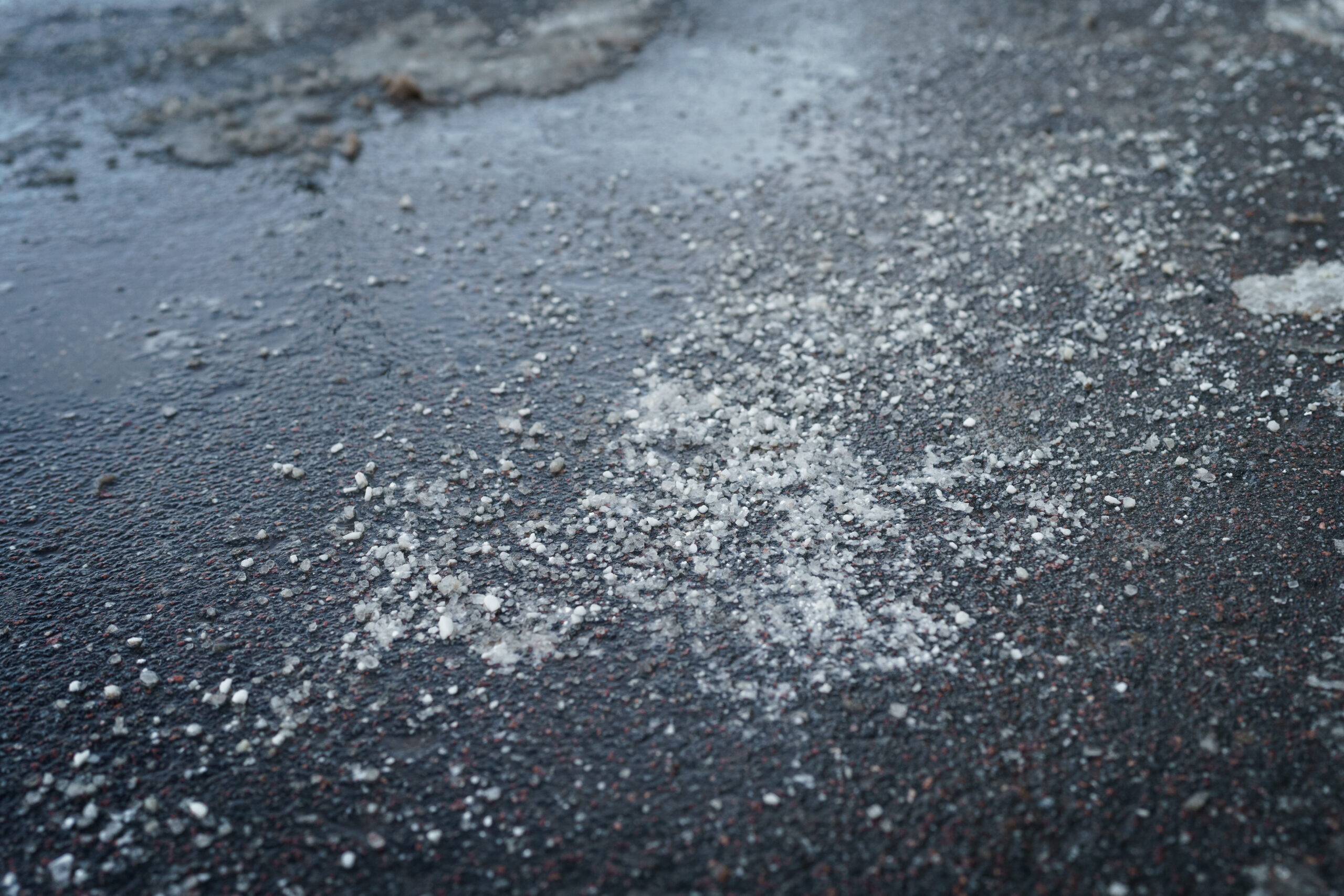 De-icing chemicals reagent on aspåhalt. Pavement is sprinkled with technical salt or salt mixtures based on it. Effective tool to fight ice on roads in winter season. .