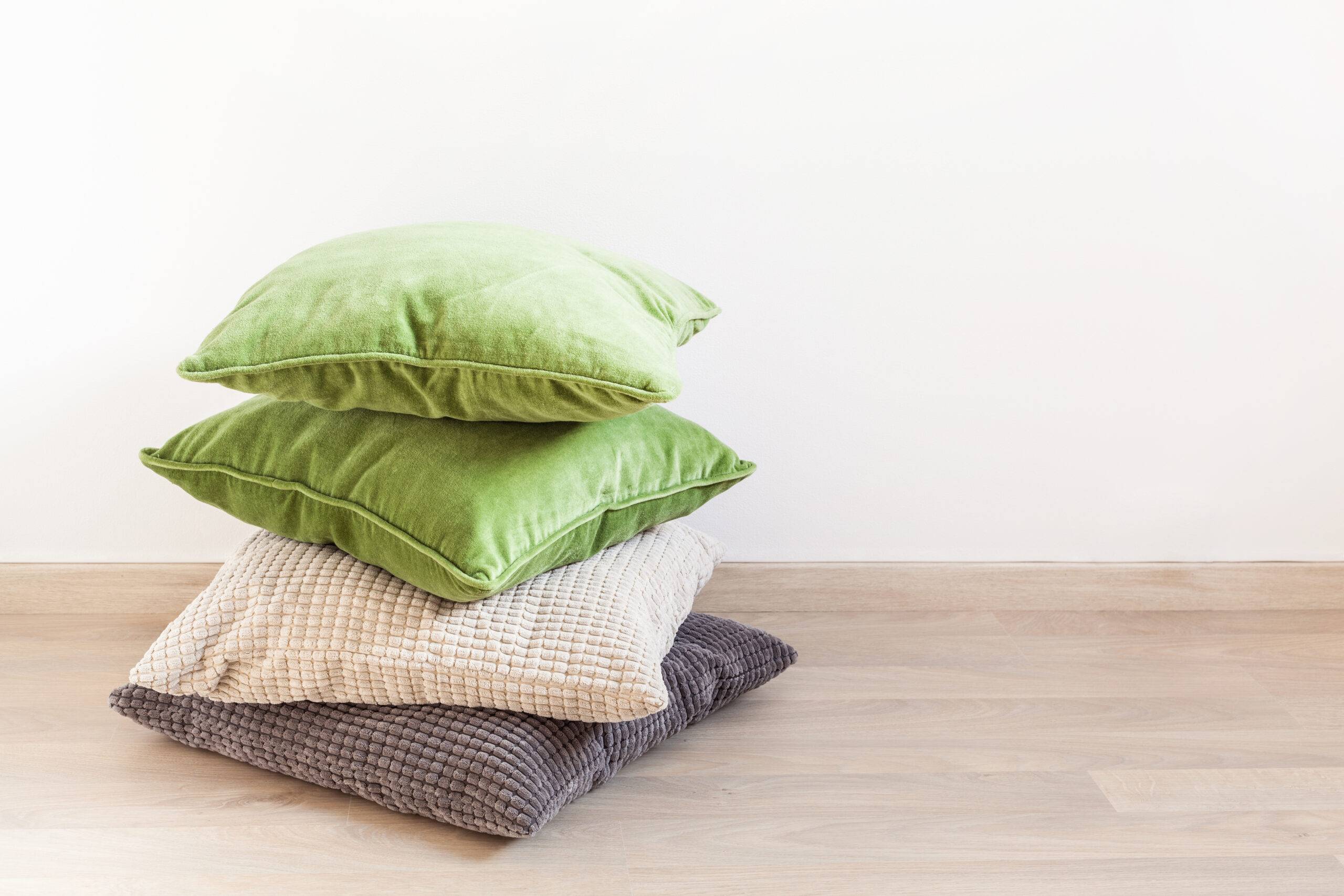 A stack of throw pillows, in green, grey, and cream, stacked on the floor.