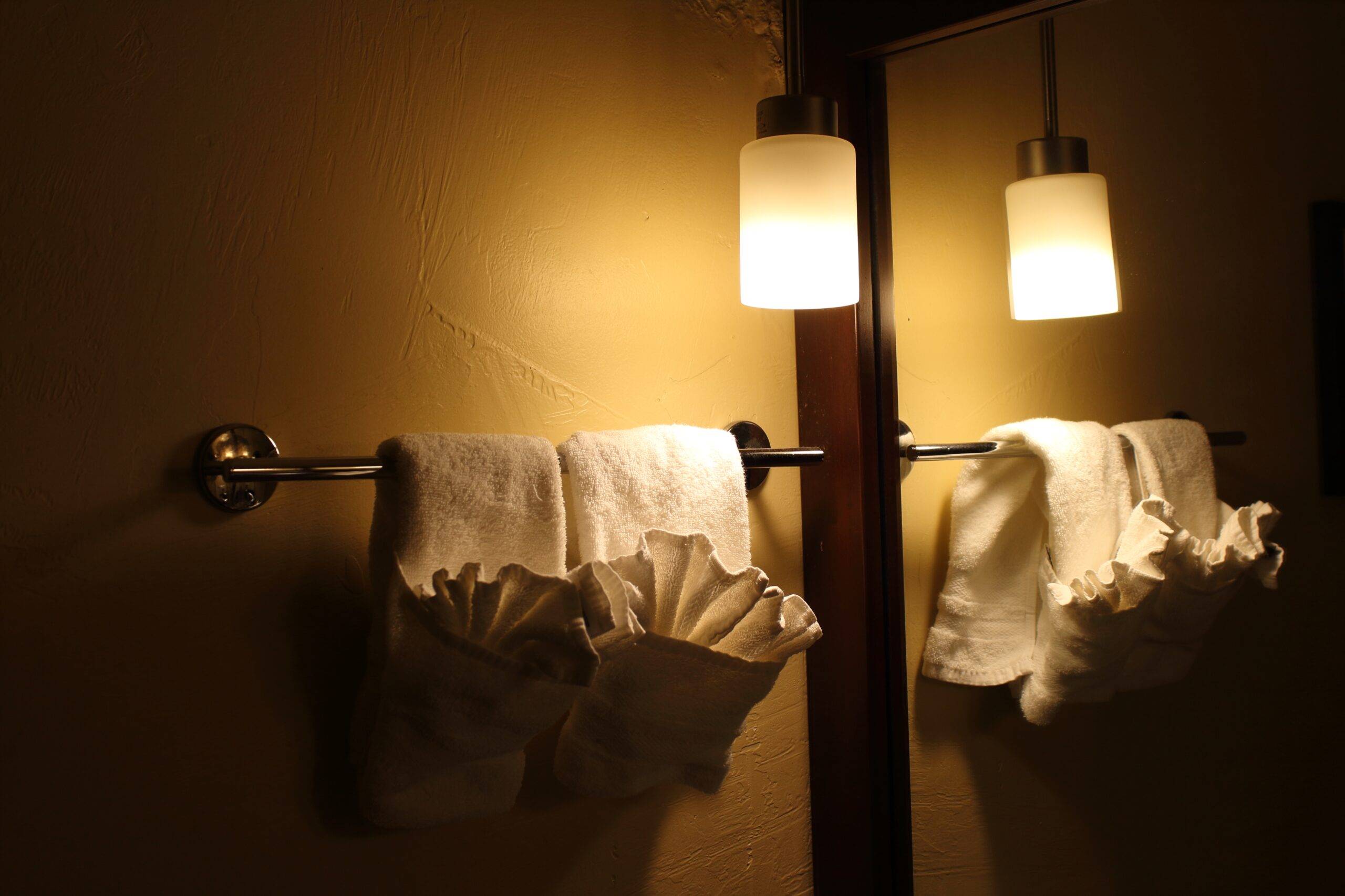 A dramatic wall lamp lighting a corner of a bathroom above a towel rack.