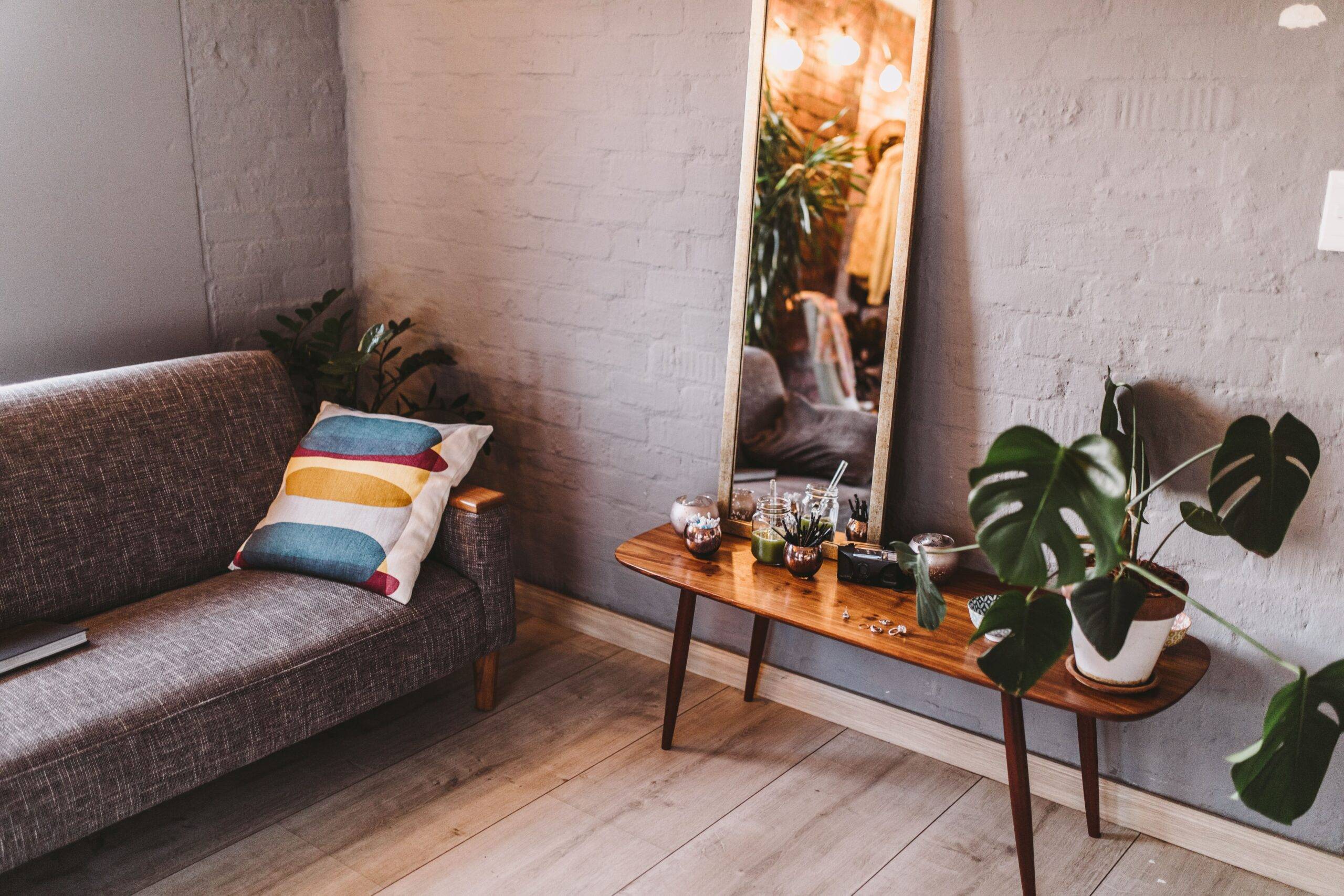 A corner of a living room showing the edge of a couch and a table against the wall with a tall mirror atop it.