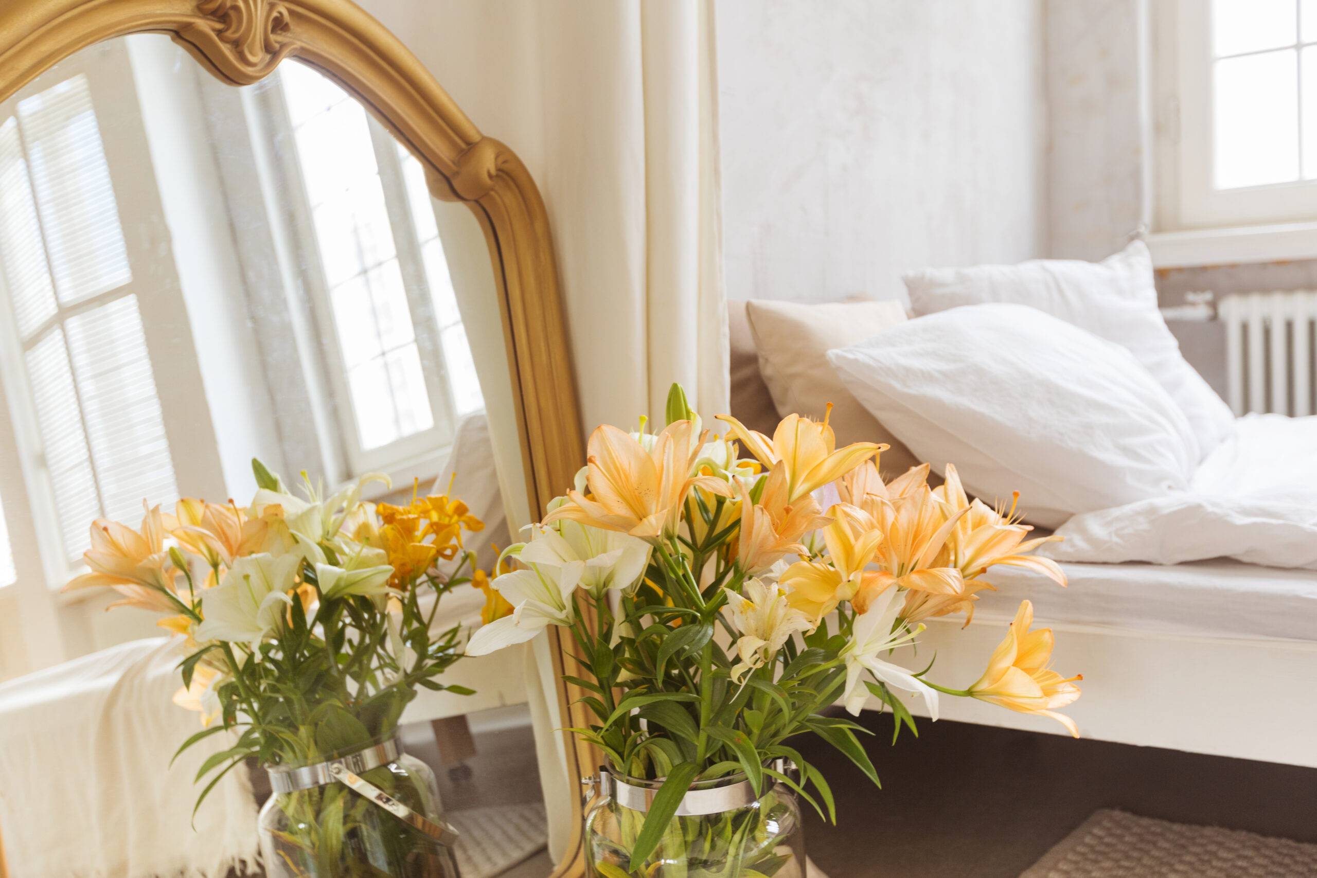 Bouquet of lilies flowers and mirror placed near curtain and comfortable bed in elegant bedroom at home