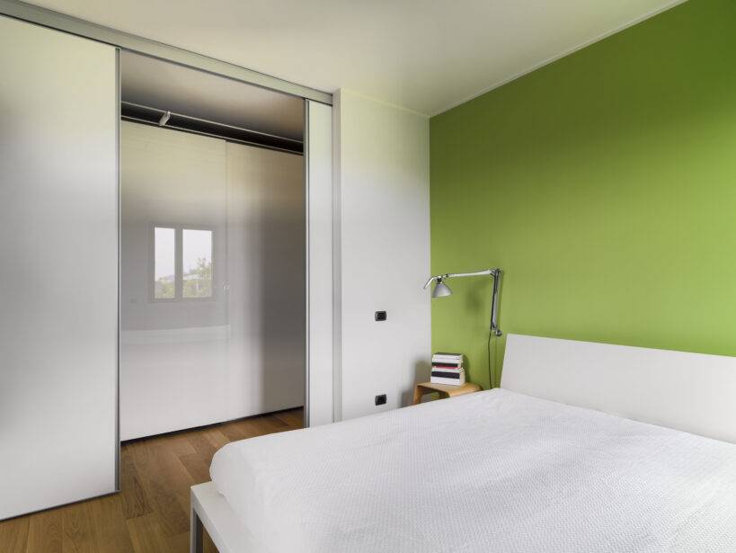 interior view of a modern bedroom with wood floor whose wall is painted of green overlooking on the corridor