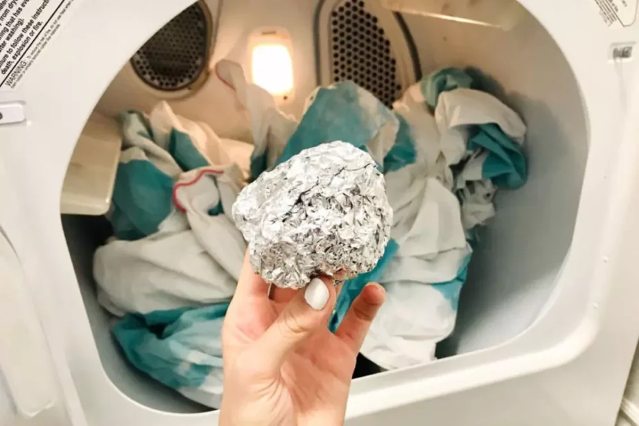 A hand holding up a balled up piece of tinfoil in front of an open dryer.