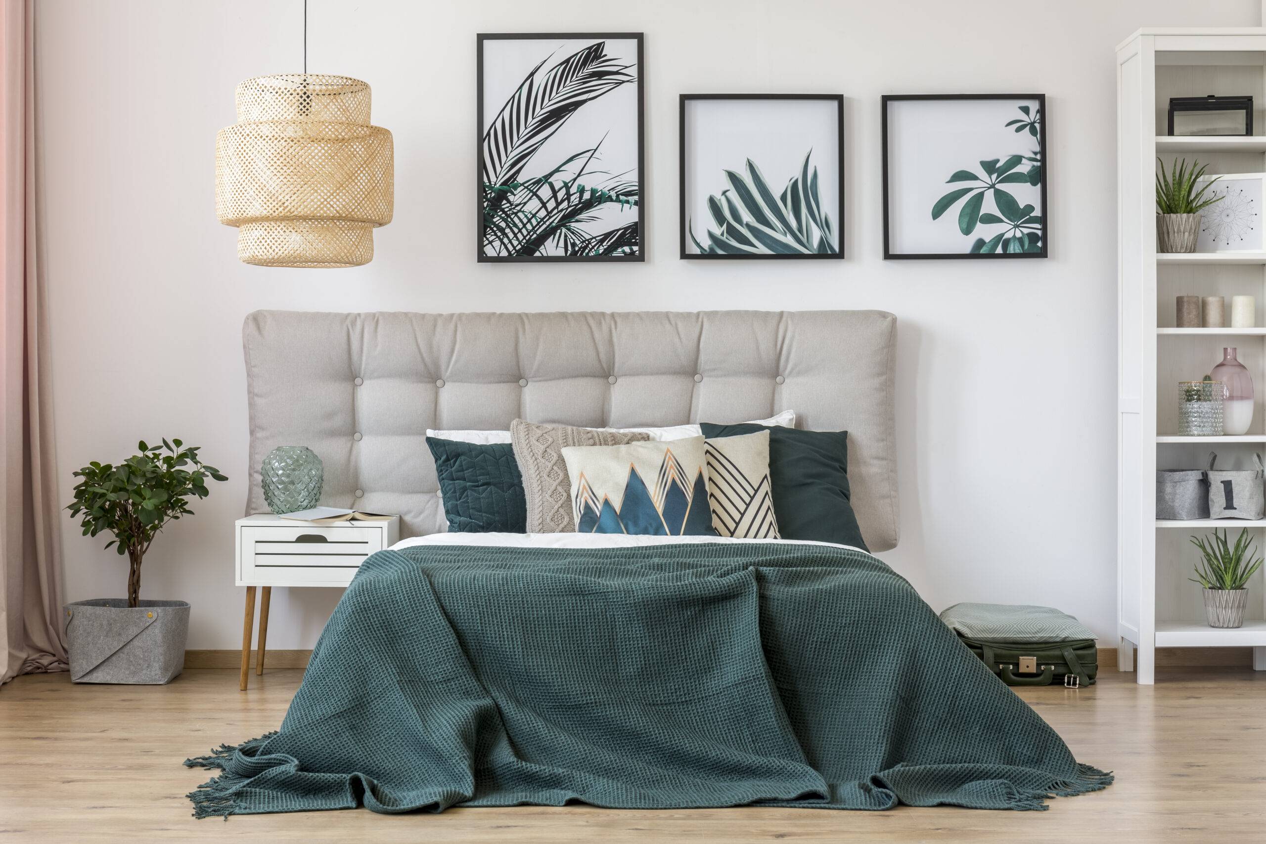 Rattan lamp above bed with green bedding and grey bedhead in bedroom interior with leaves posters