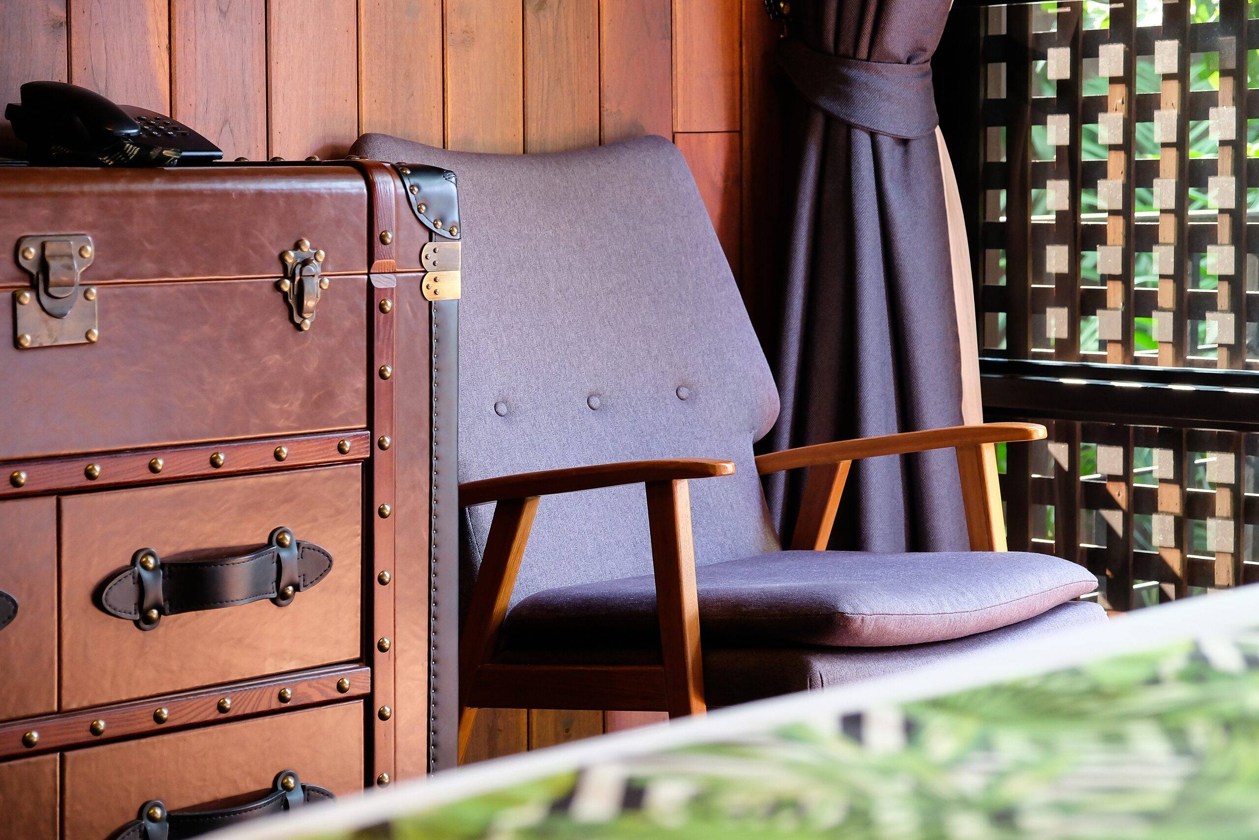 A close shot of some vintage furniture, a mid-century-modern chair and a more antique trunk-style dresser.