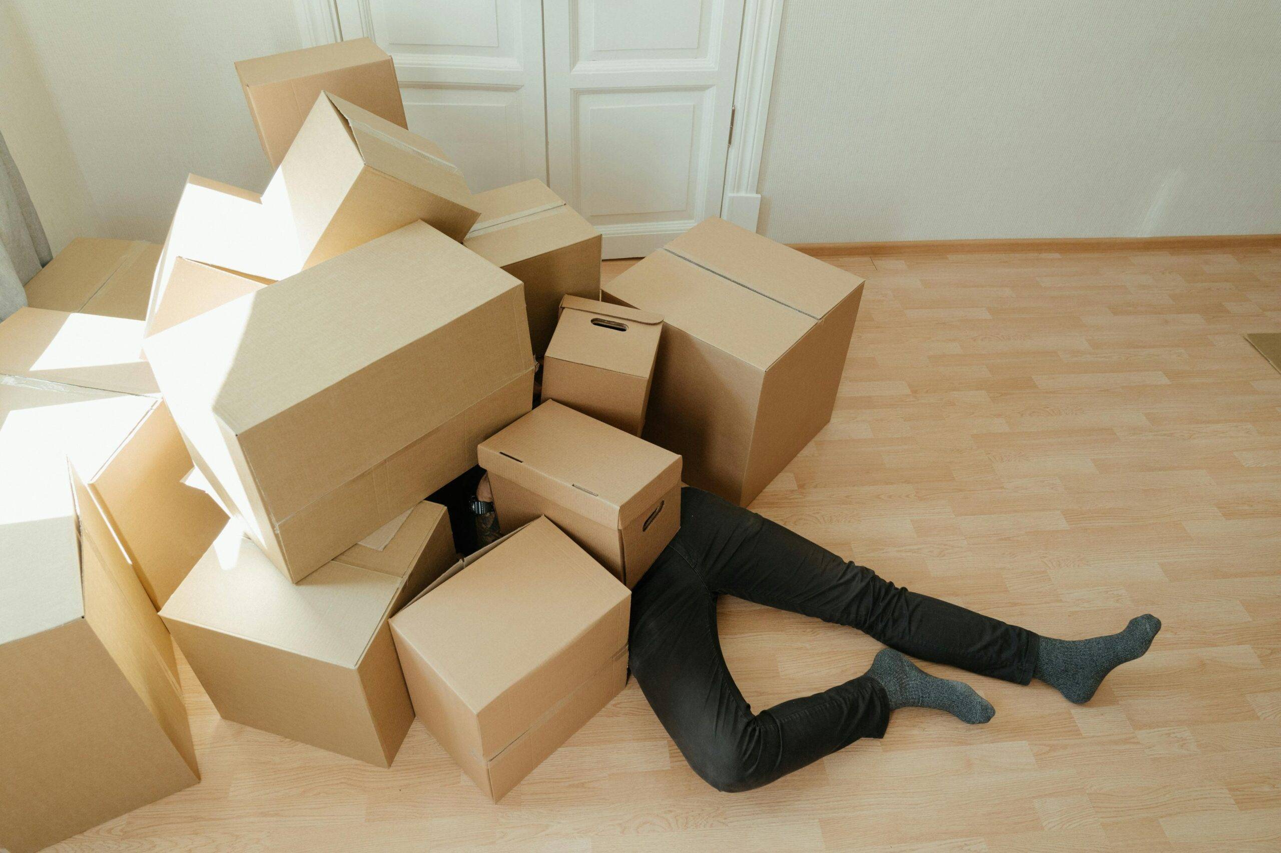 Someone laying beneath a bunch of moving boxes, their legs sticking out.