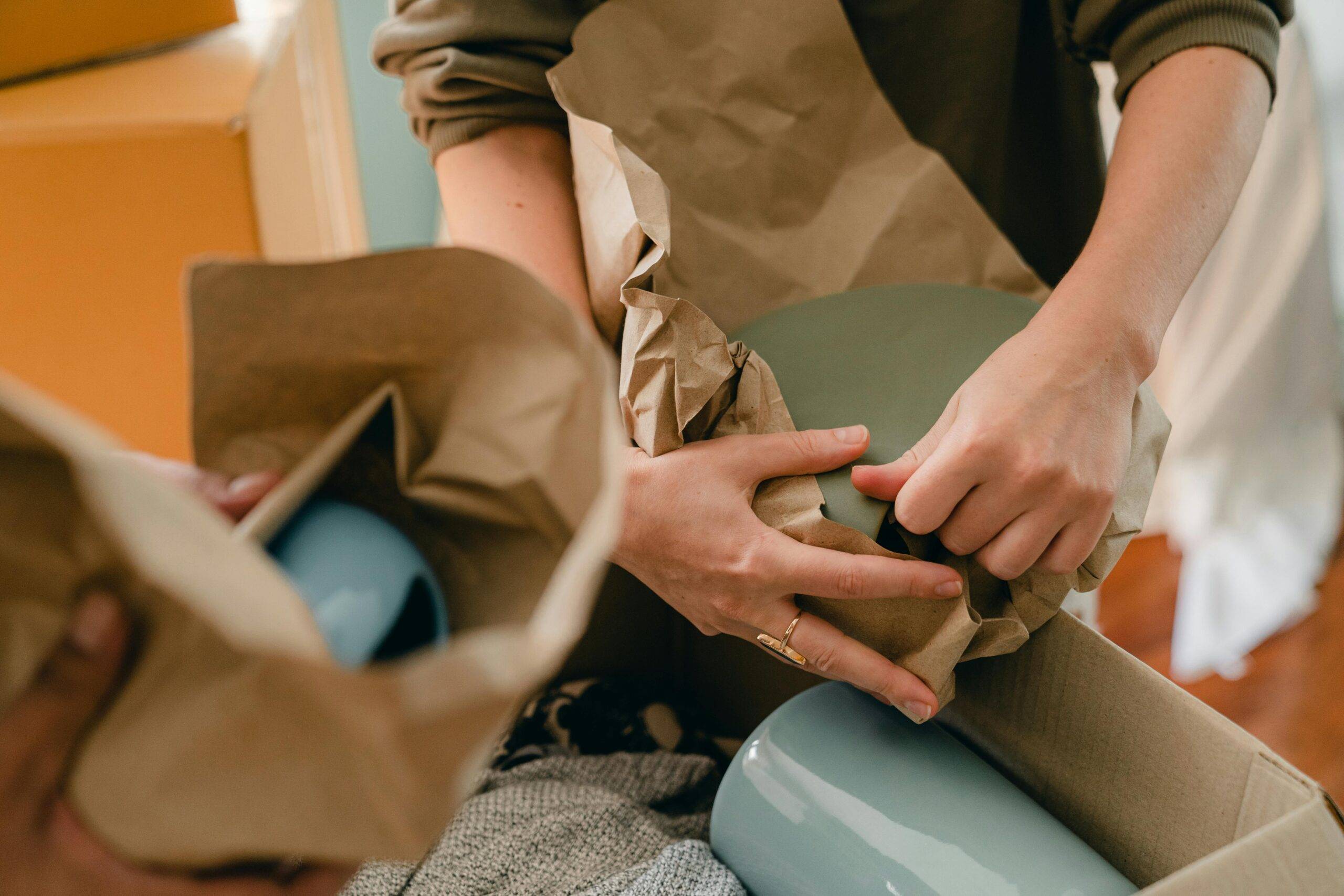 Two people wrapping dishes to put them in a box.