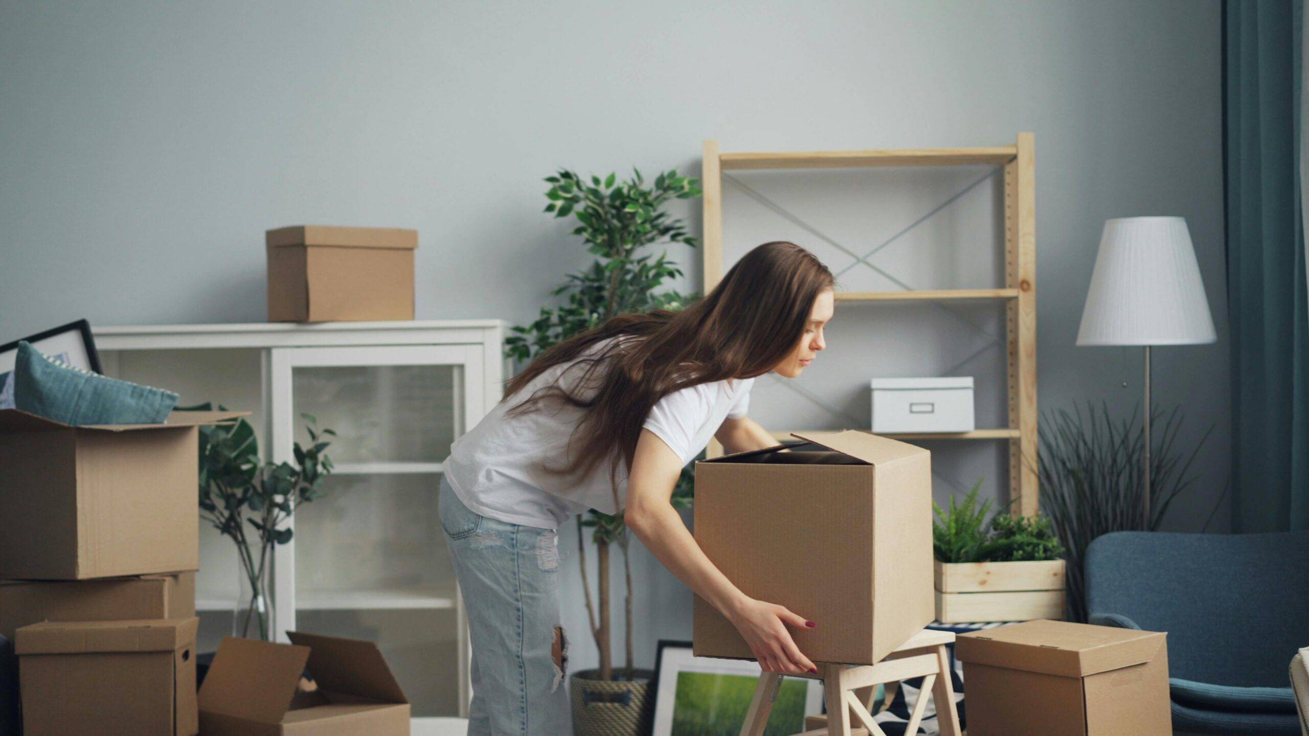 A woman bending over to place a moving box on a table.