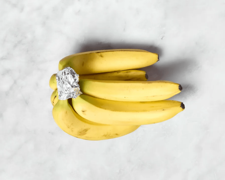 A bunch of bananas on a marble countertop with tin foil wrapped around the joint stems.