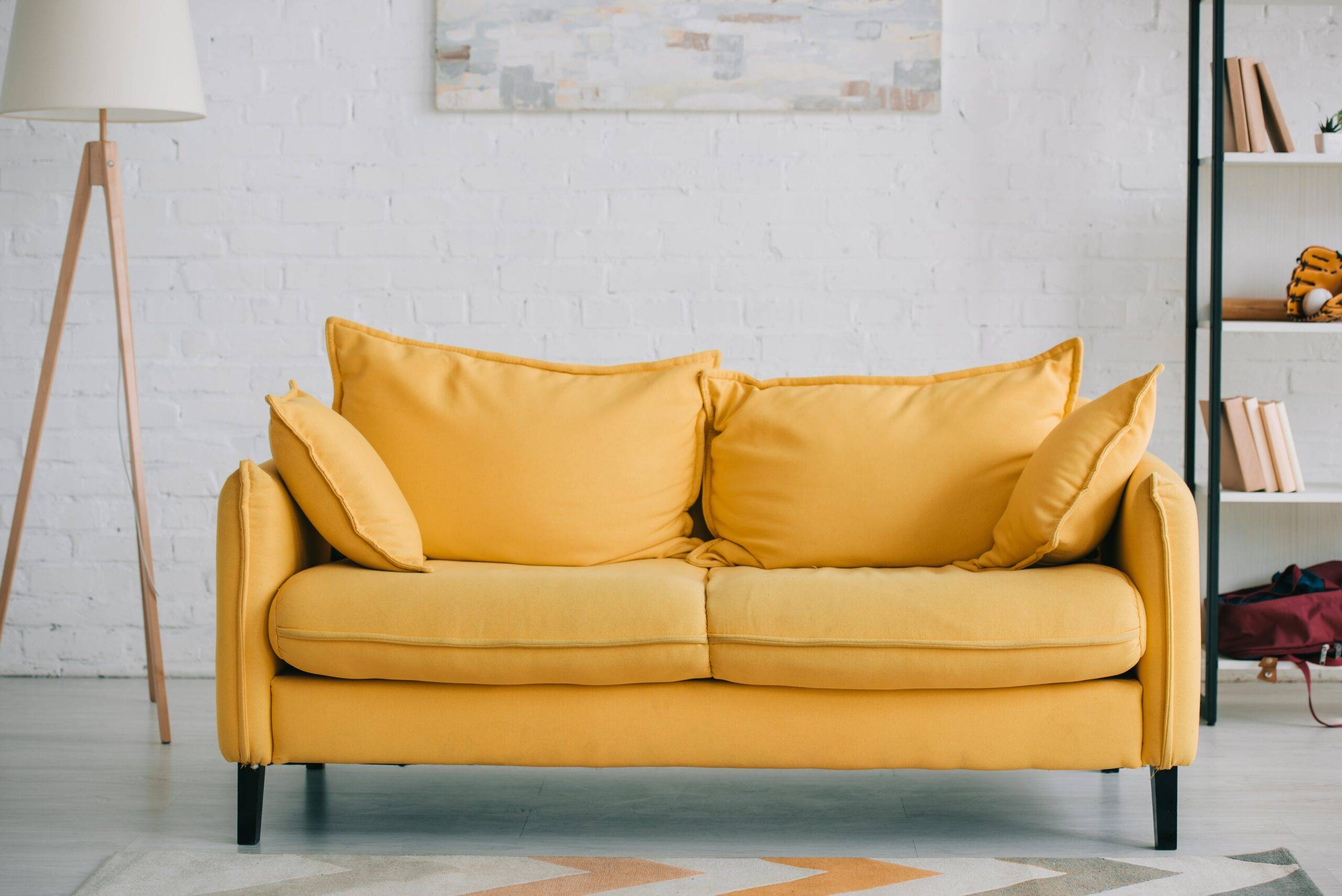 A small, yellow couch in an otherwise white room.