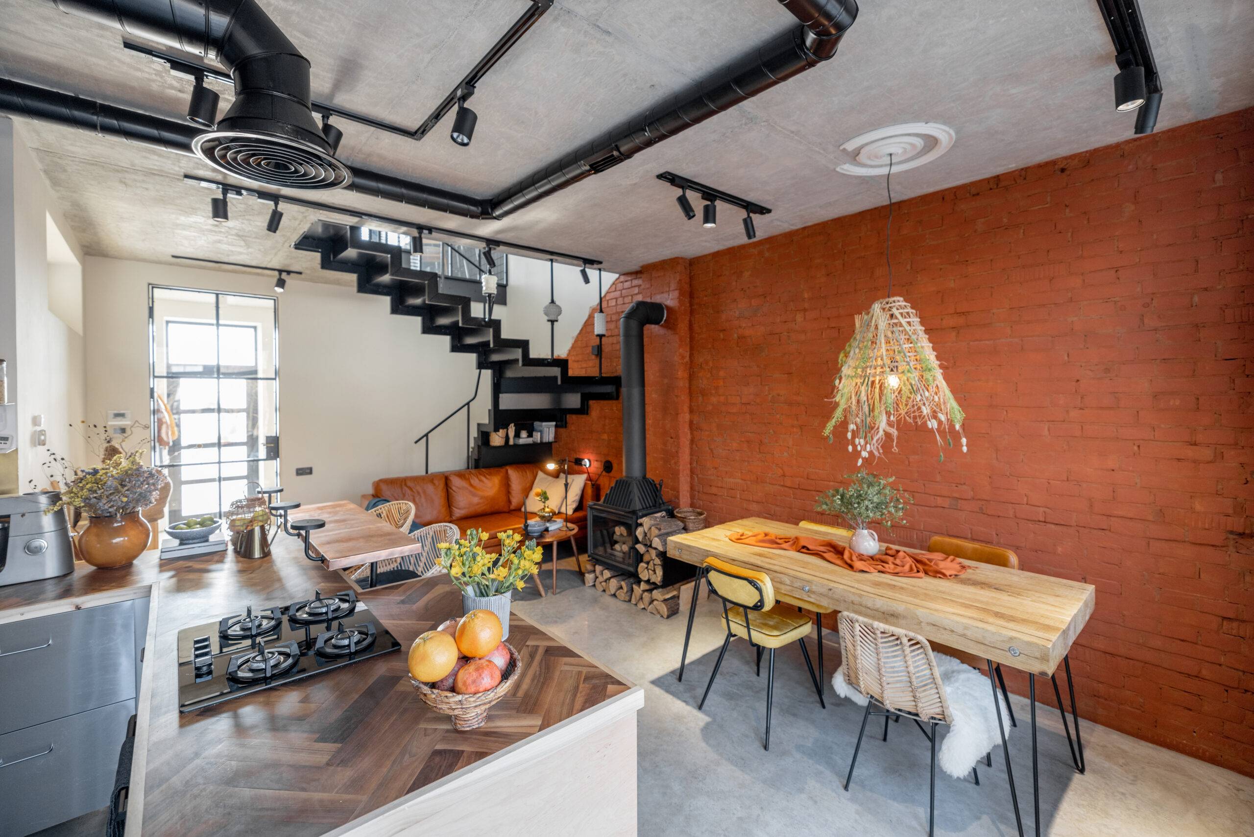 Stylish house living room interior in mixed style with the use of natural materials in finishing and furniture. Brick wall, concrete floor, ceiling, metal stairs, wooden table