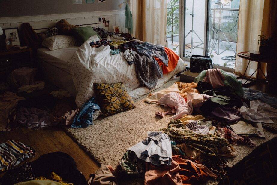 A messy bedroom, clothes strewn on the bed and floor.