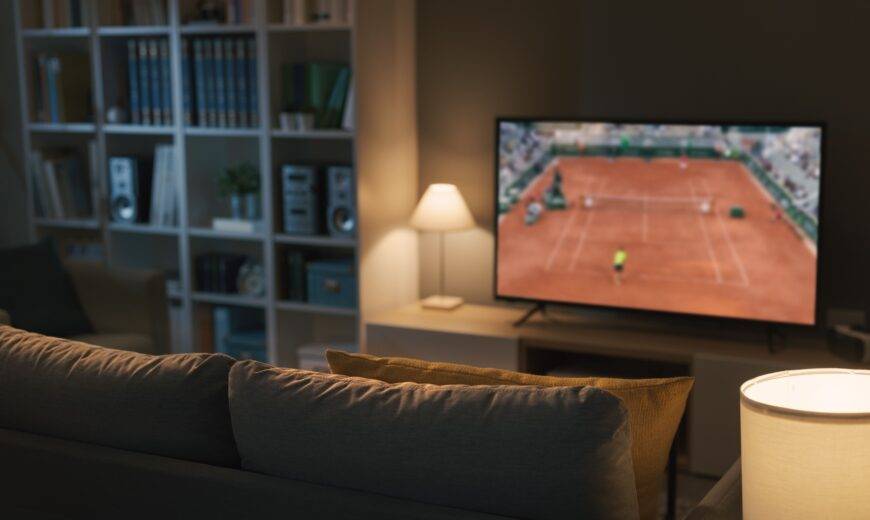 A couch facing a TV that's playing a tennis game.