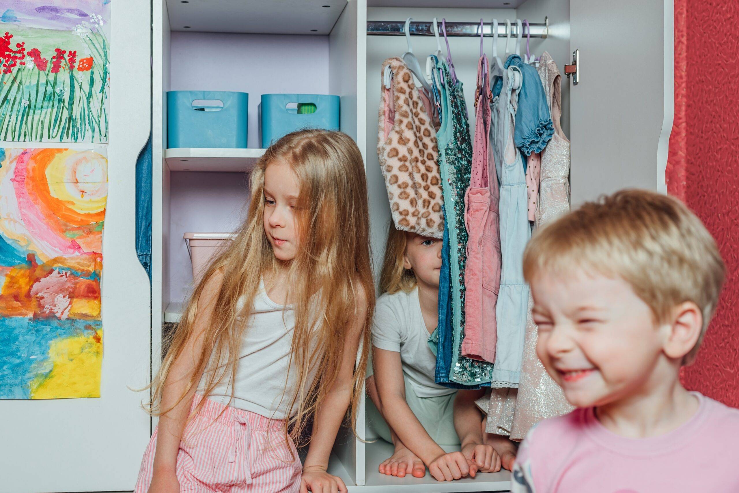 child twins play, laugh, have fun, hide at home in the closet with clothes