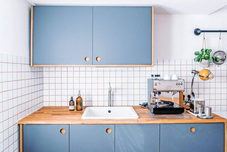 A minimalist, modern kitchen with dusty blue cabinets and wood finishes.