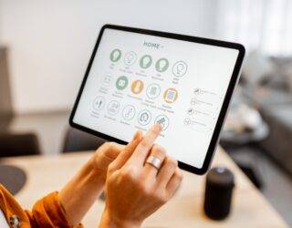 A woman holding up a tablet with a number of smart home controls up on the screen.