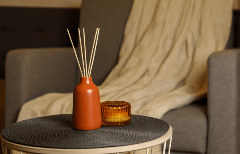 A small orange vase holding a bundle of reed diffusers.