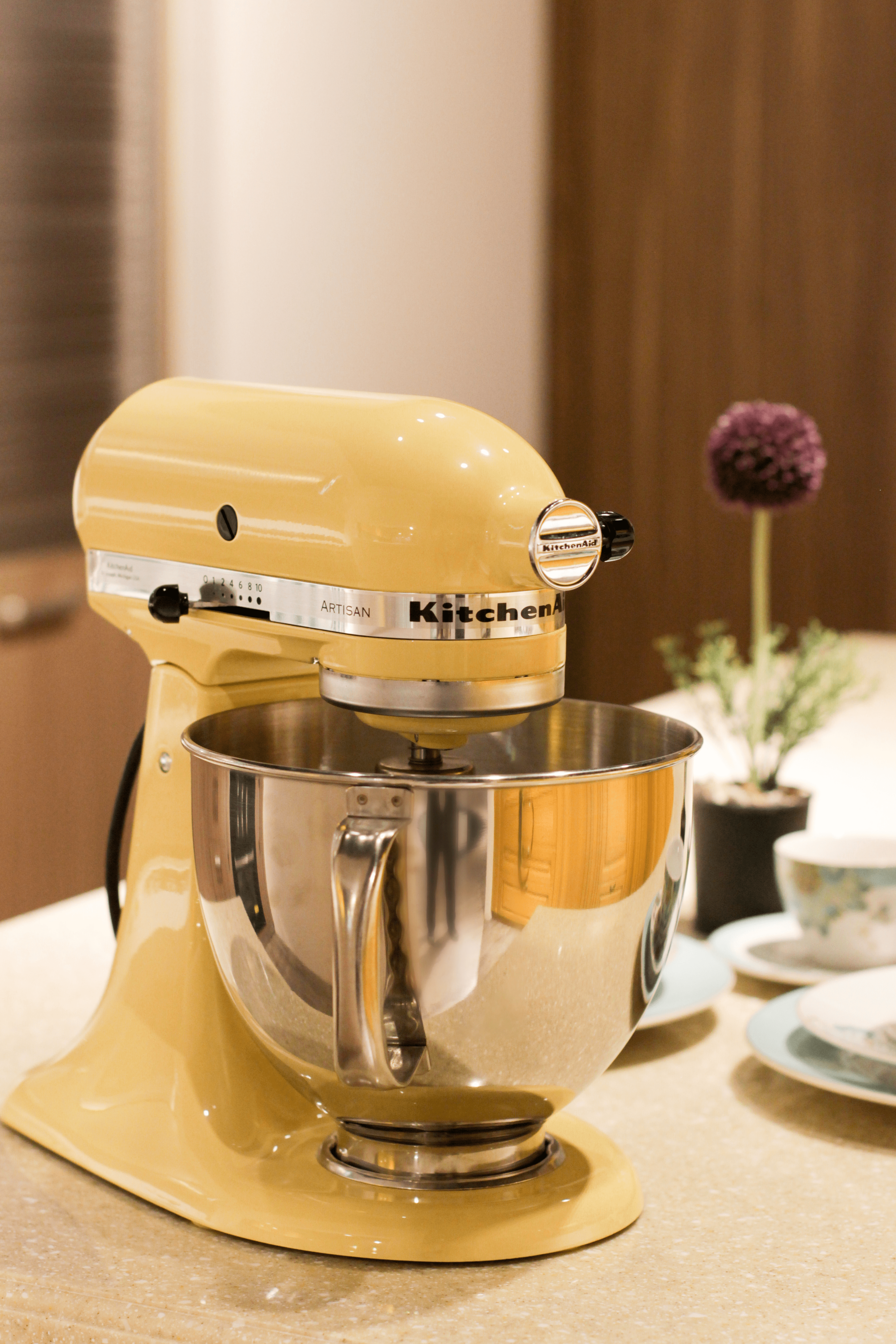 Mixer KitchenAid kuning di atas meja.