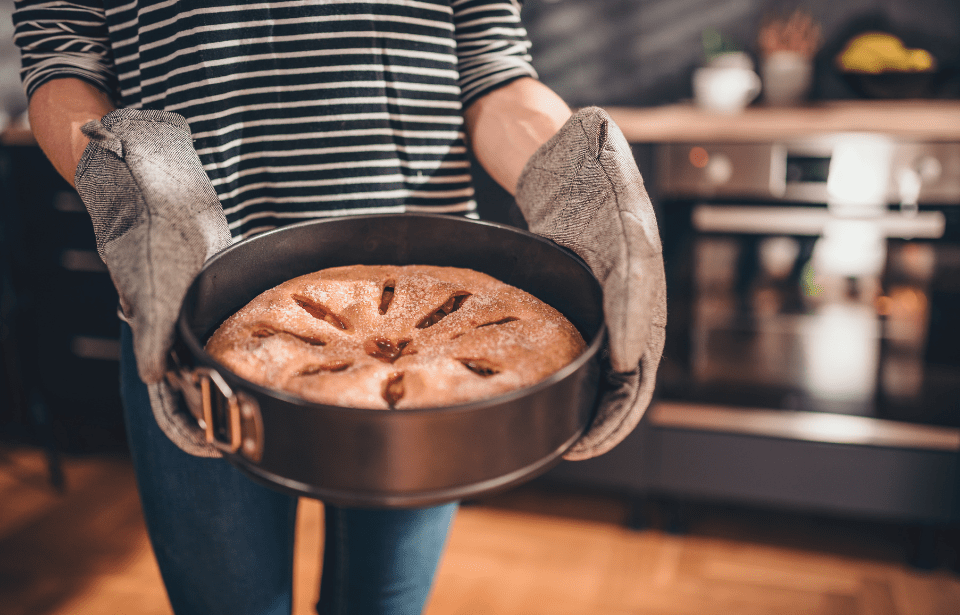 Someone holding a pie in a tin, wearing oven mitts, having just removed it from the oven.