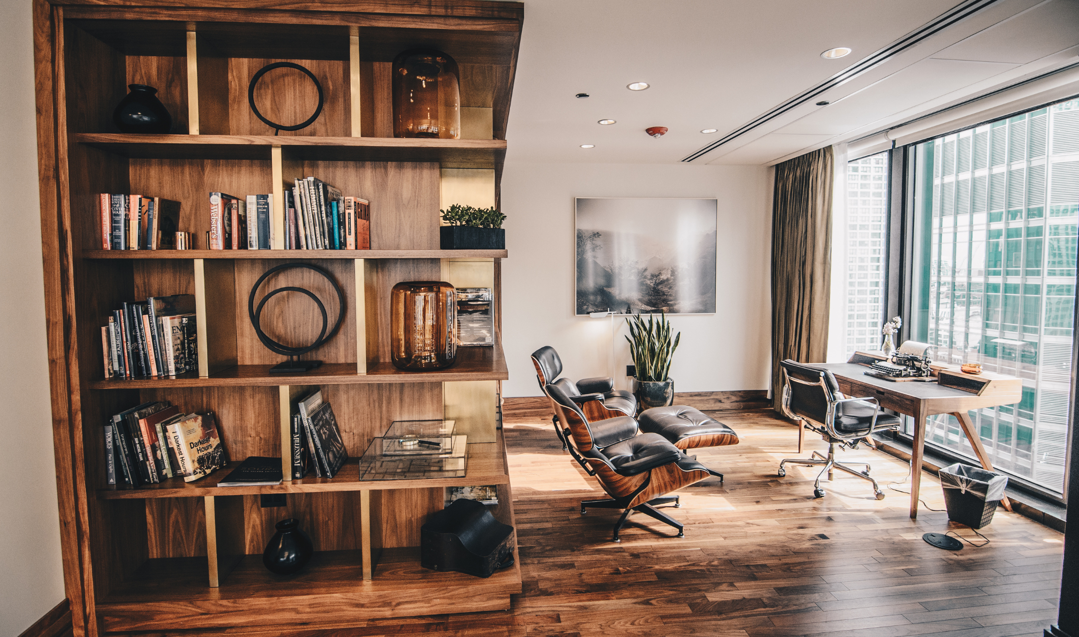 A large floor to ceiling bookcase in an office, filled with books and sculptural elements.