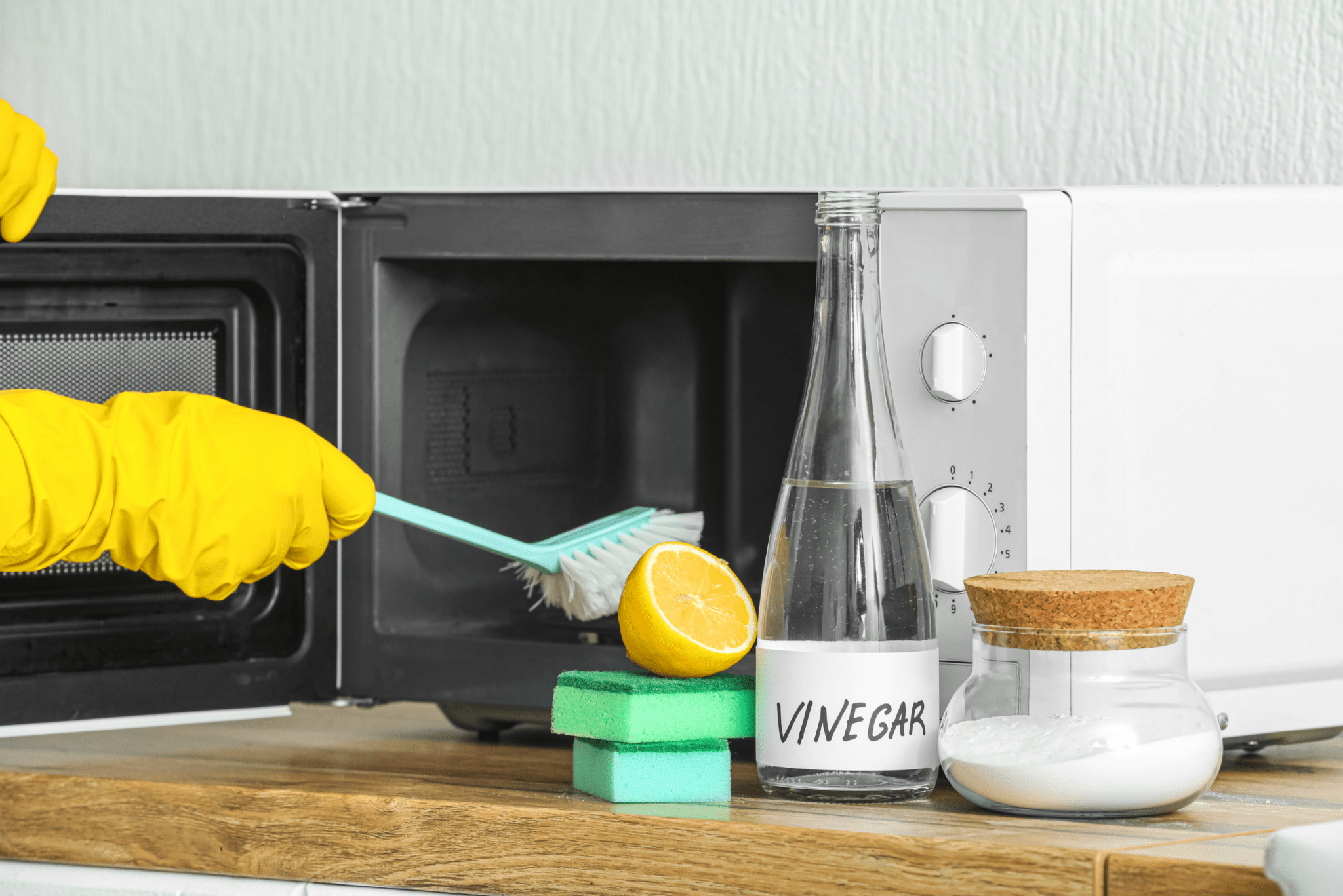 Someone cleaning out their microwave, a bottle of vinegar and a jar of baking soda next to them.