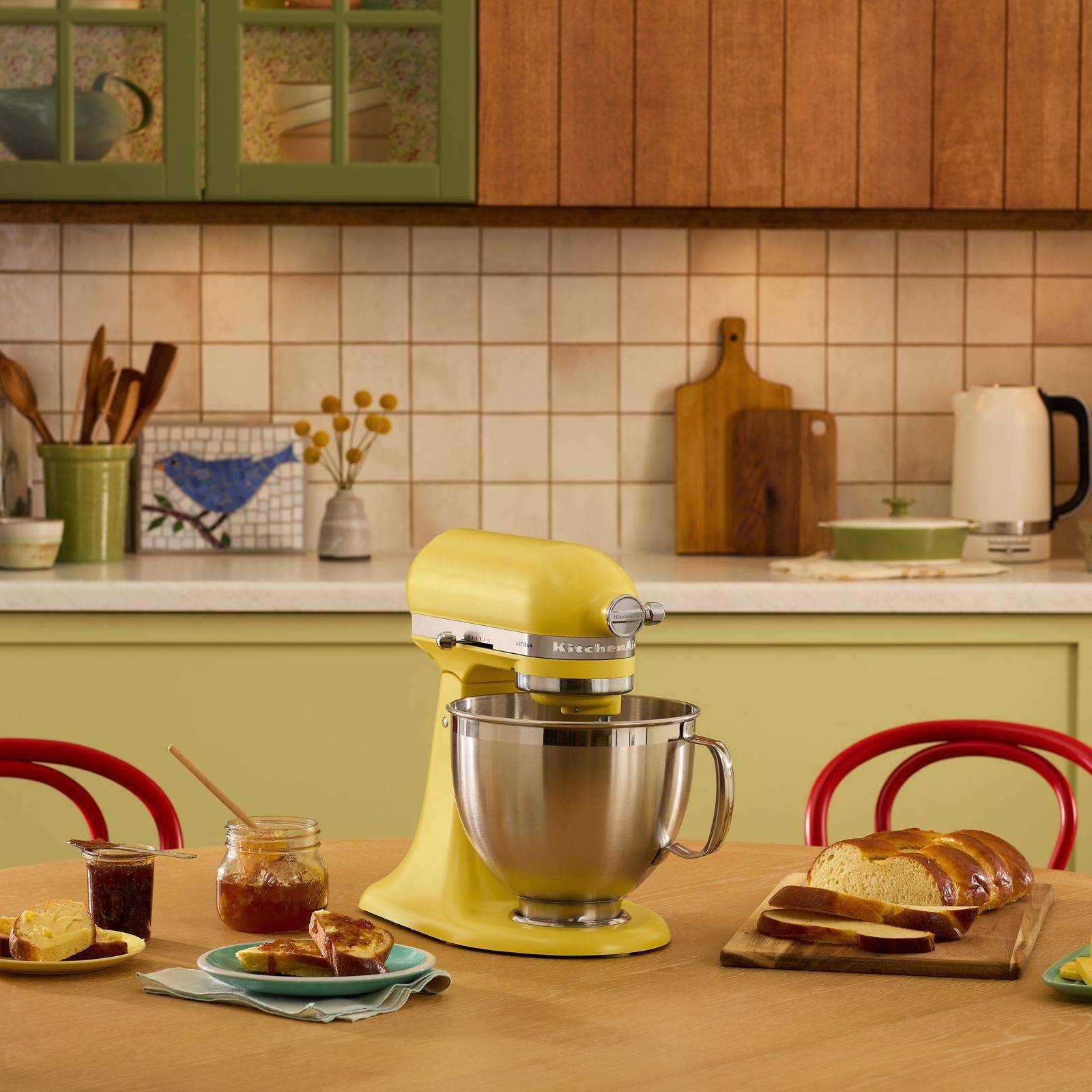 A yellow kitchenaid mixer on a kitchen table amid some breakfast foods.