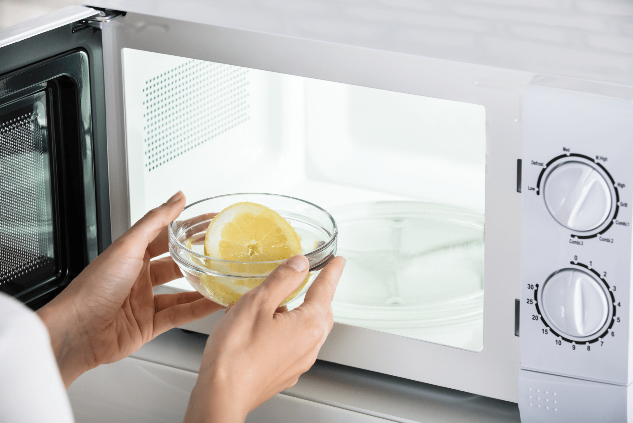 Someone placing a bowl with half a lemon in it into a microwave.